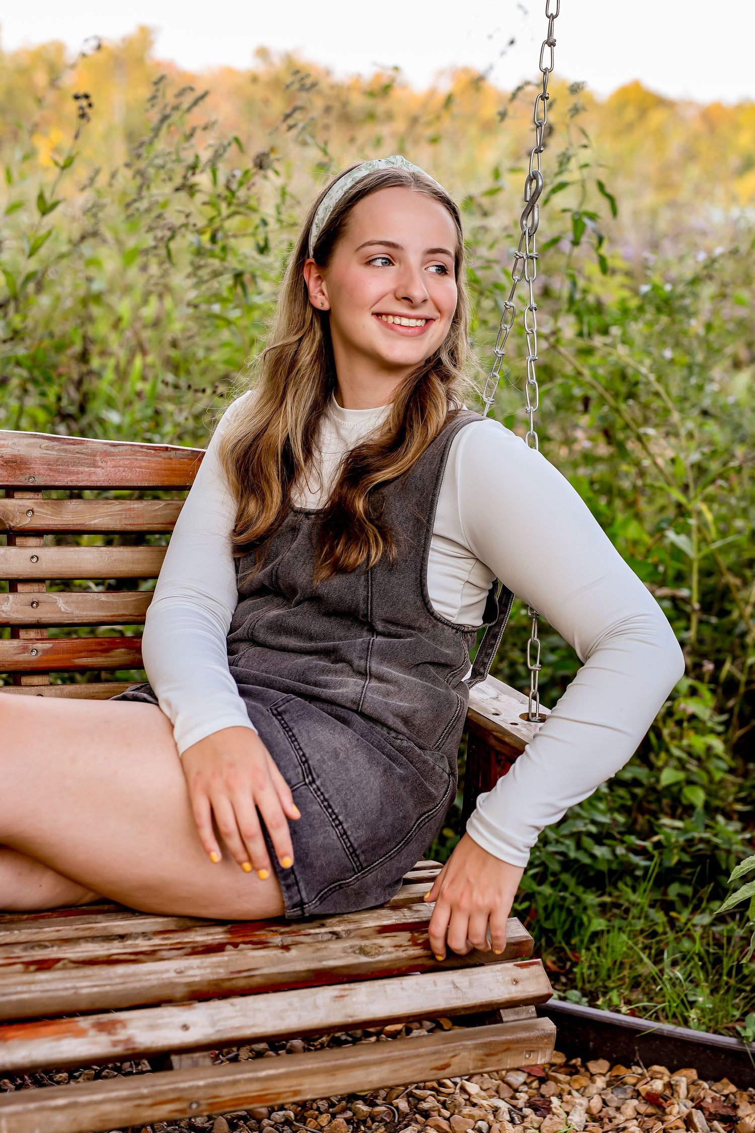 Casual outdoor portrait session on wooden bench surrounded by fall foliage.
