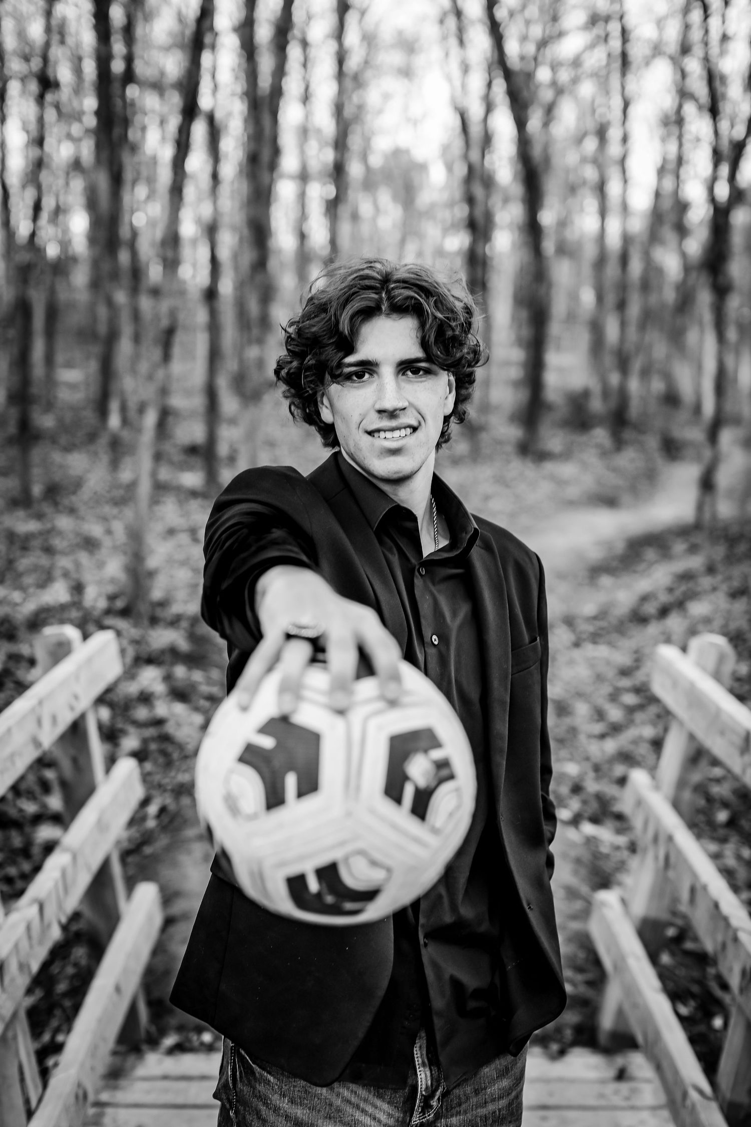 Black and white portrait on wooden bridge holding soccer ball.