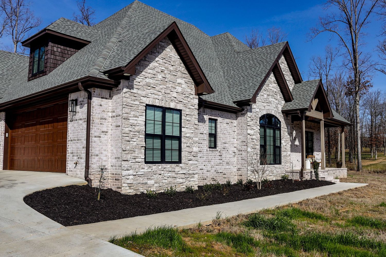 Modern stone and wood craftsman style house with multiple gables and dormers against blue sky.