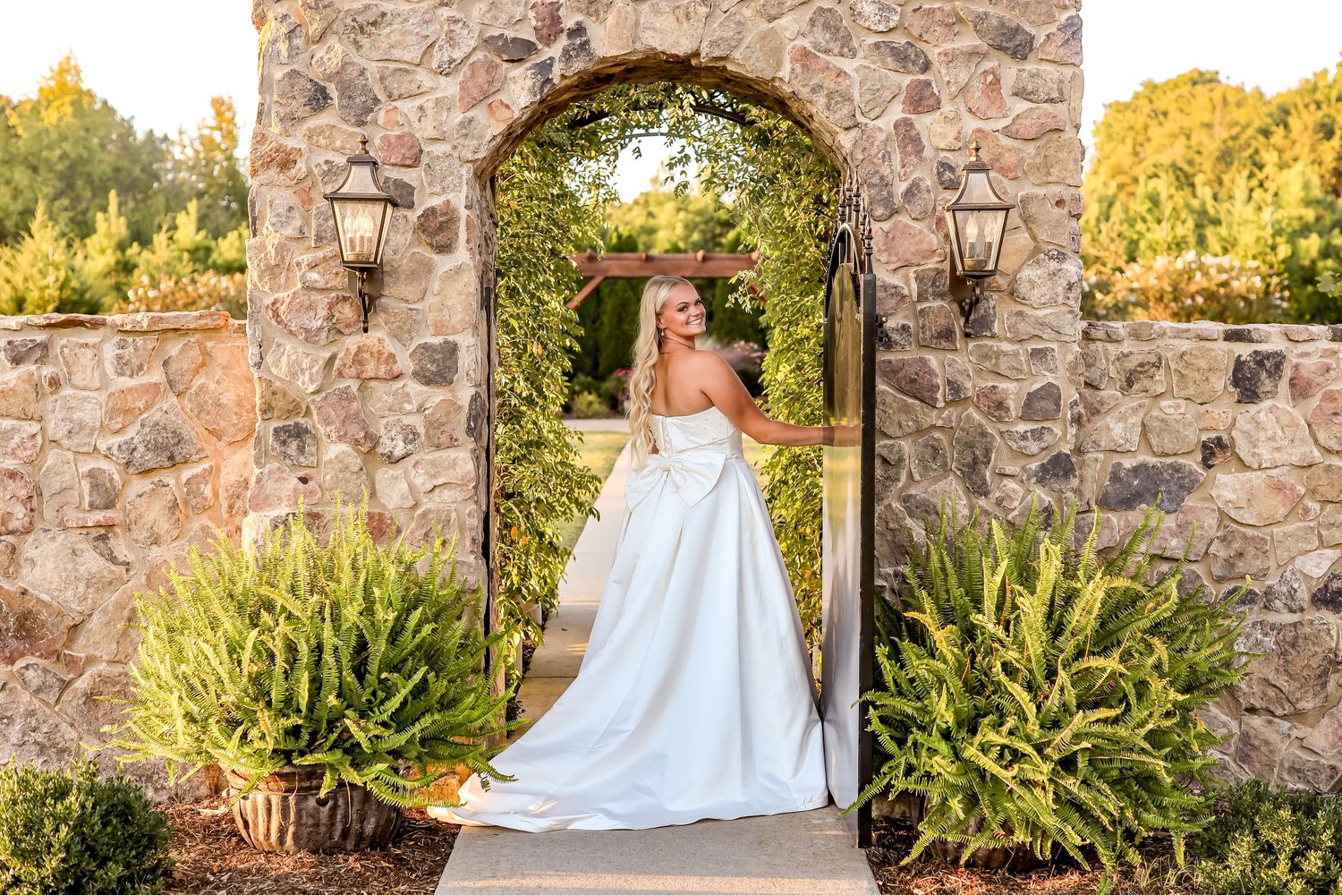 A bride in a white ballgown poses against rustic stone walls during golden hour.