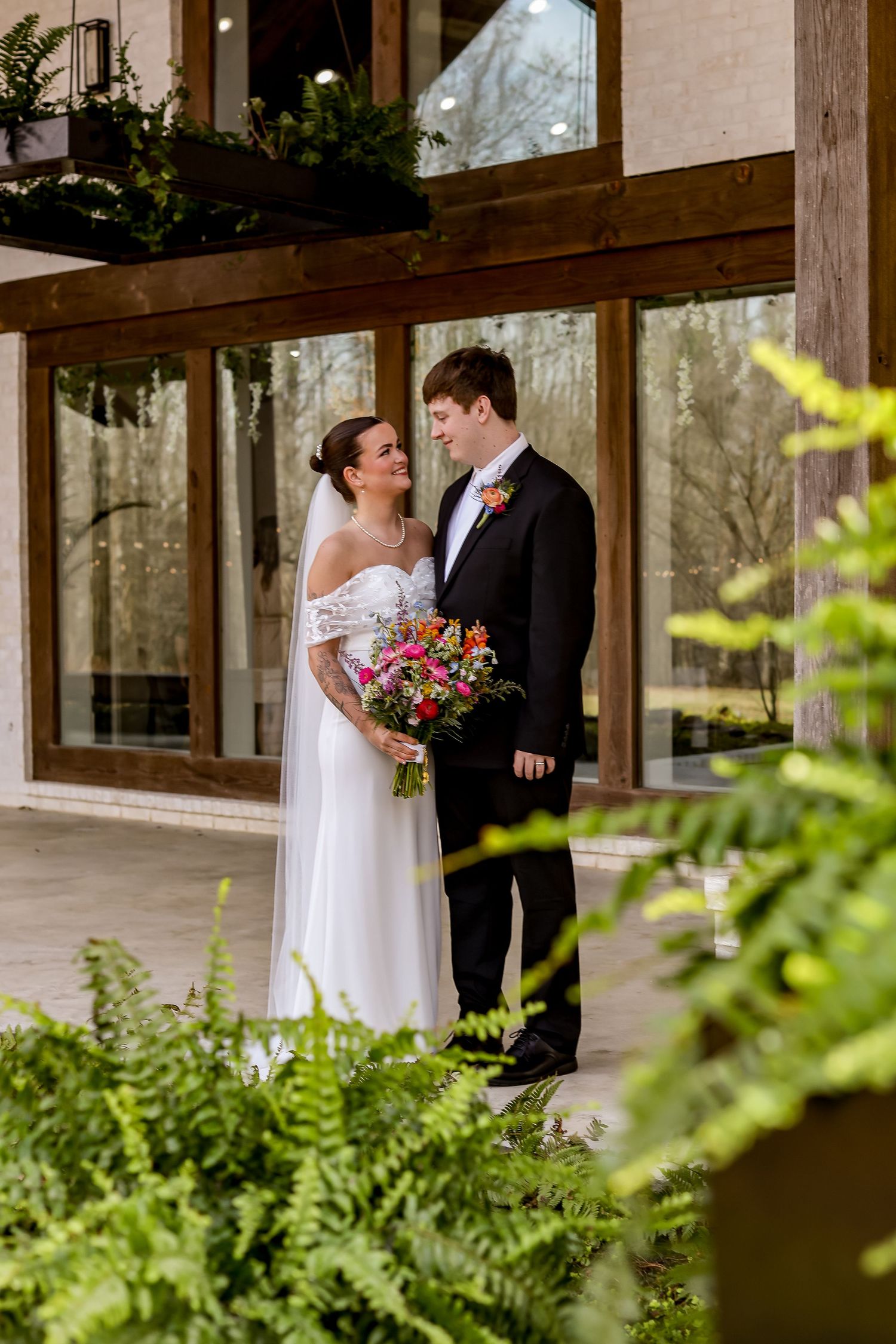 Wedding couple shares intimate moment under covered walkway with lush greenery and natural lighting.