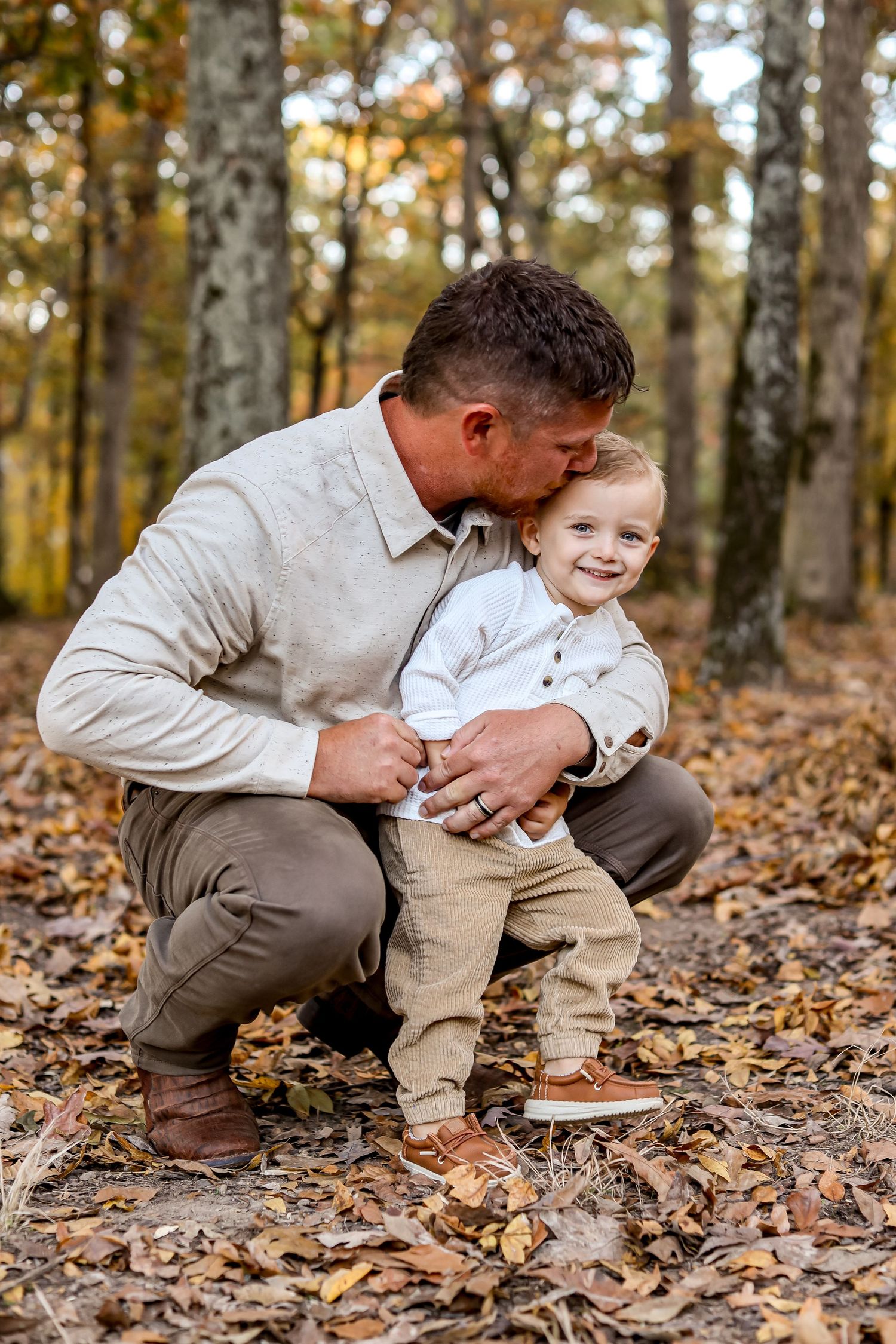 Playful interaction between parent and child among fallen autumn leaves in wooded setting.