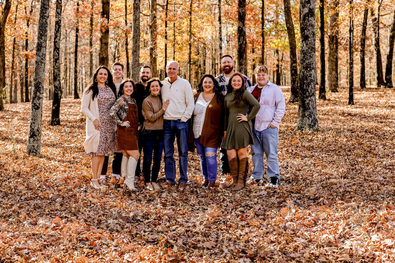 Large family group photo taken in autumn forest with fallen leaves.