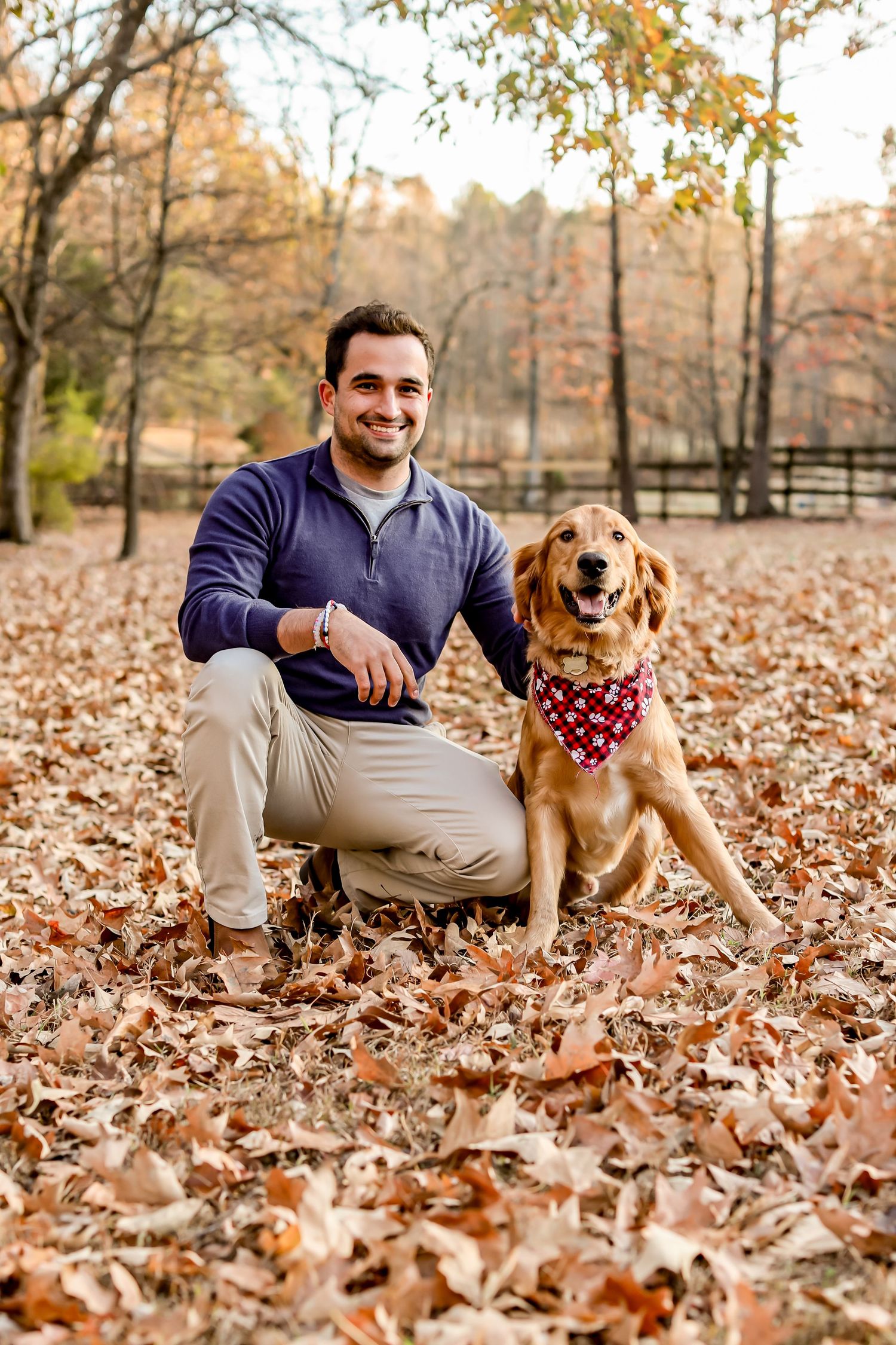 Golden retriever wearing a bandana poses with companion among fallen autumn leaves.