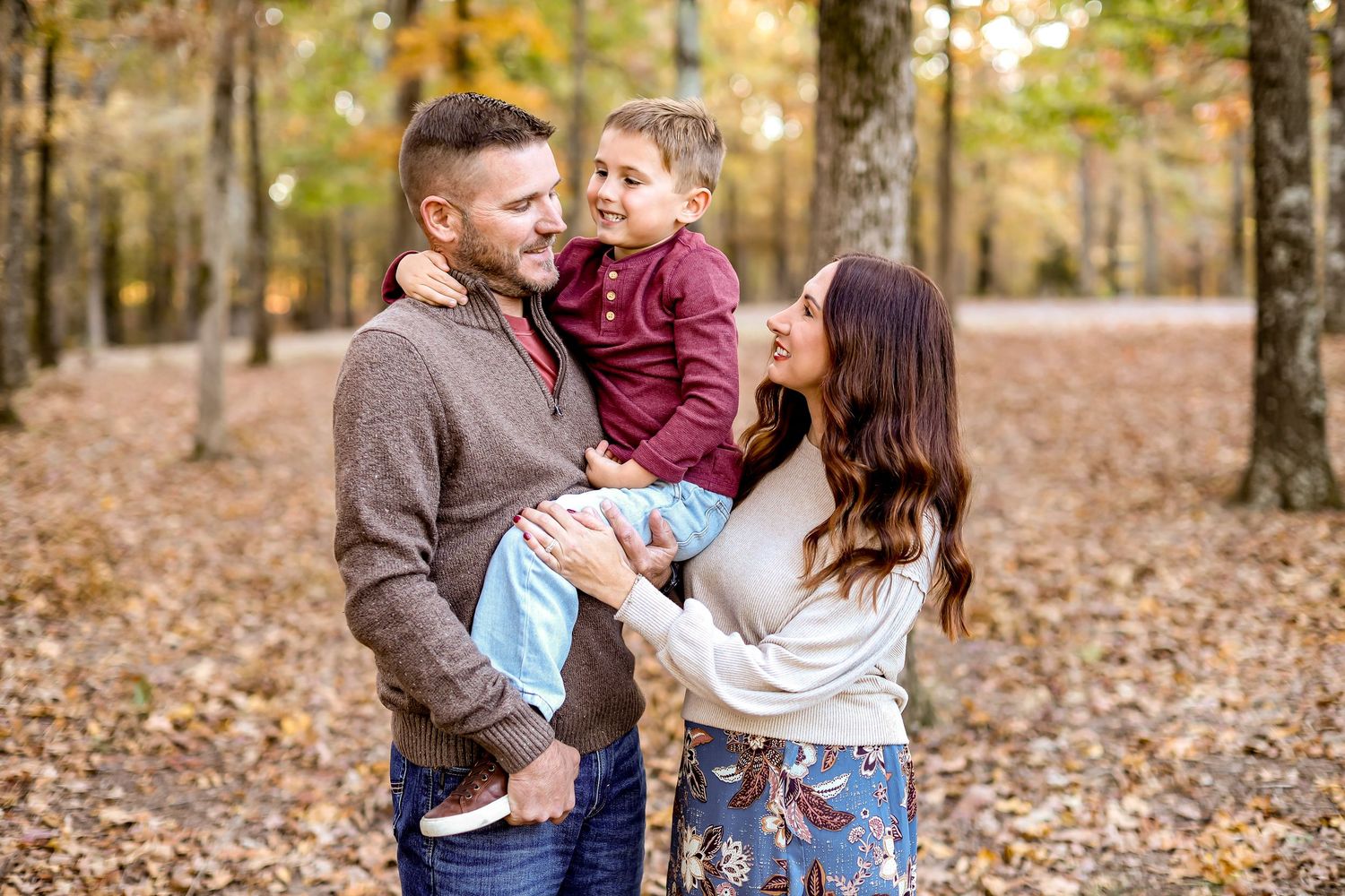 Family enjoying a fun moment together in autumn woods with golden leaves on ground.