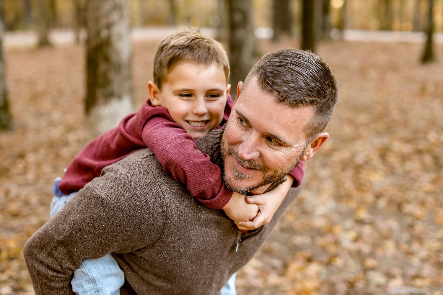 A playful piggyback ride moment captured in an autumn forest with fallen leaves.