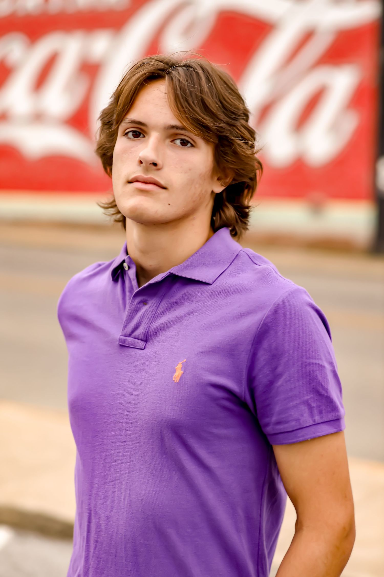Young person in purple polo shirt poses against red and white background.
