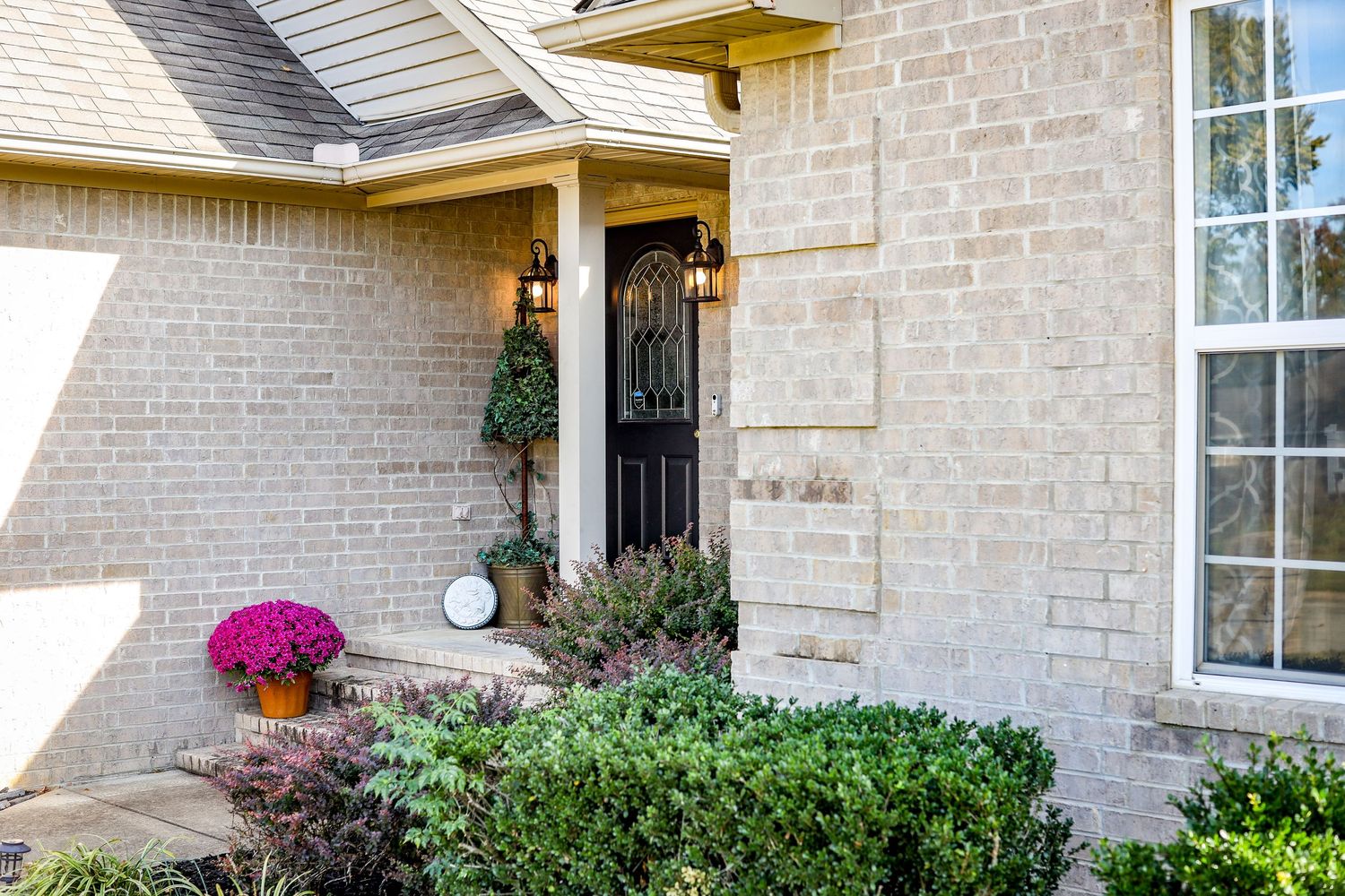 Exterior view of beige brick house with white trim and landscaped front yard.
