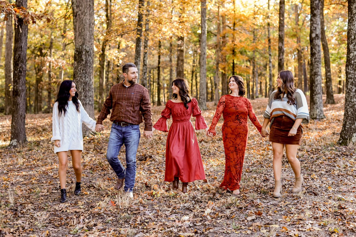 Family group walking through forest with golden fall leaves during sunset portrait session.