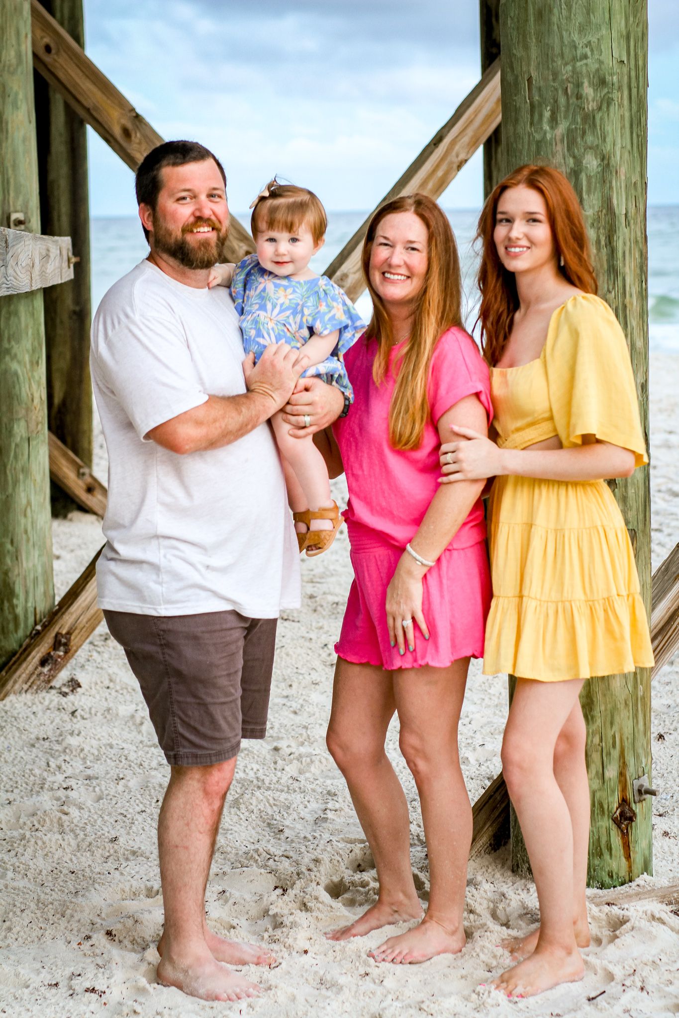 Beach portrait with wooden pier posts and bright summer outfits.