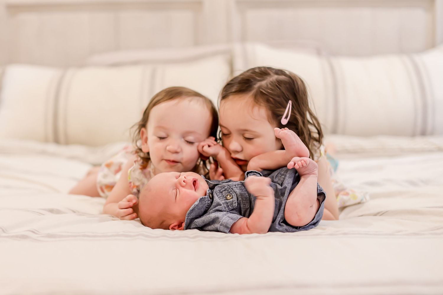 Two small children cuddle together while lying on white bedding.