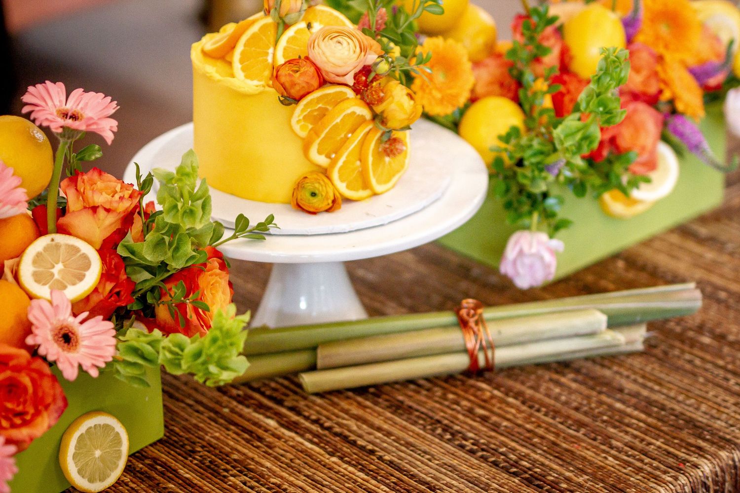 A colorful wedding dessert display featuring citrus fruits, pink flowers and yellow decor on a wooden table.