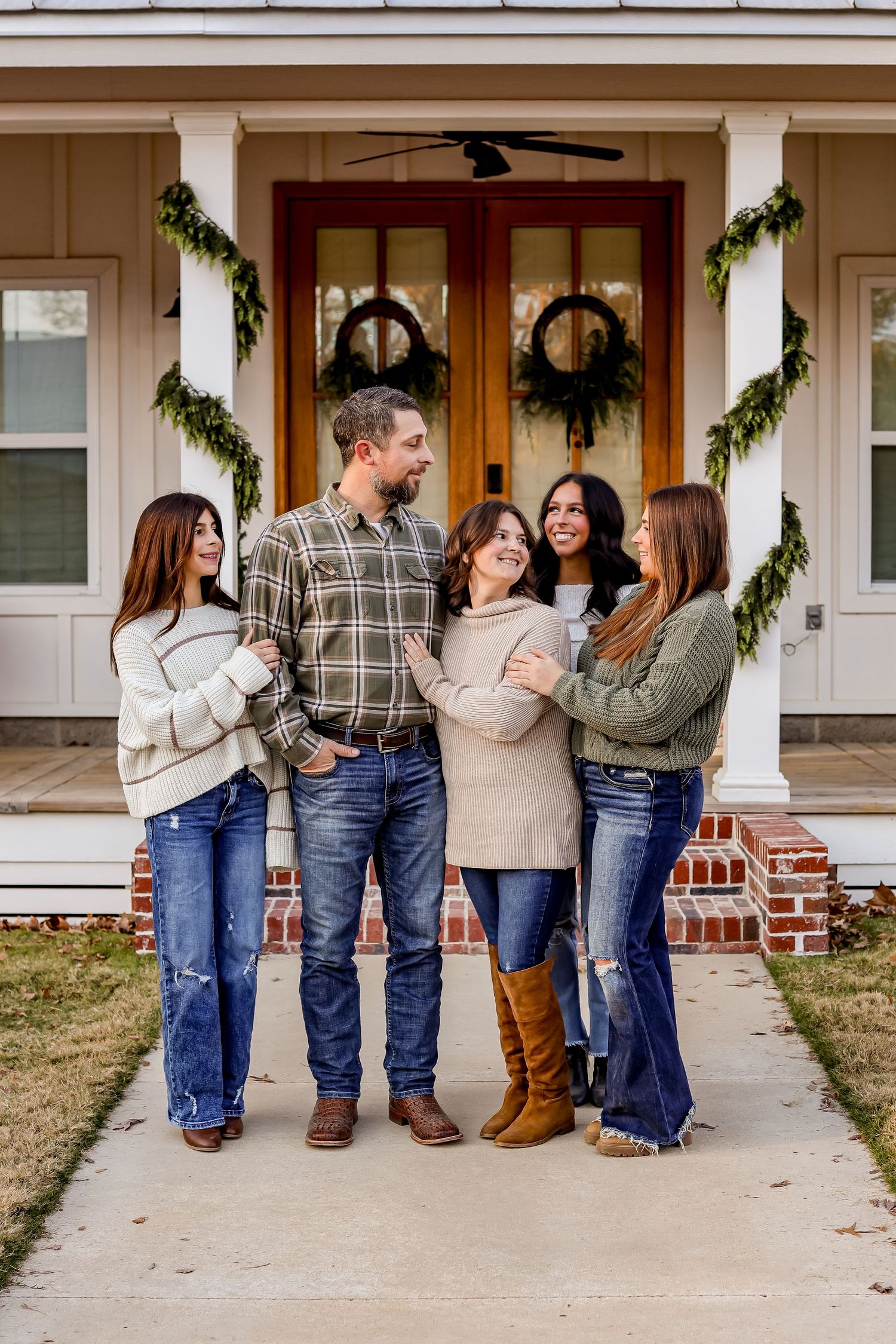 Family members sit together on a front porch step wearing coordinating casual outfits with jeans and sweaters.