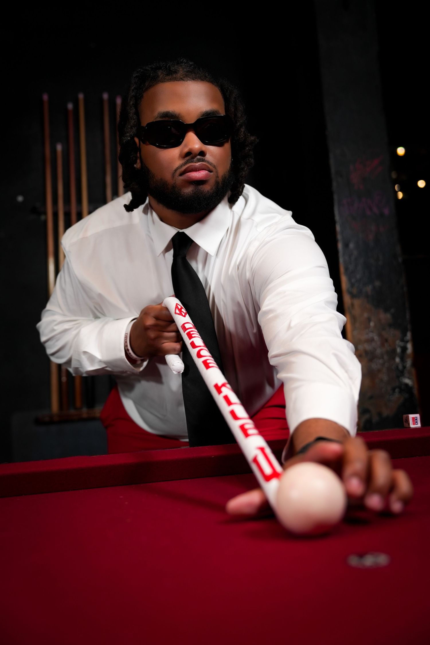 Person playing pool in white shirt at red felt table in dark room.