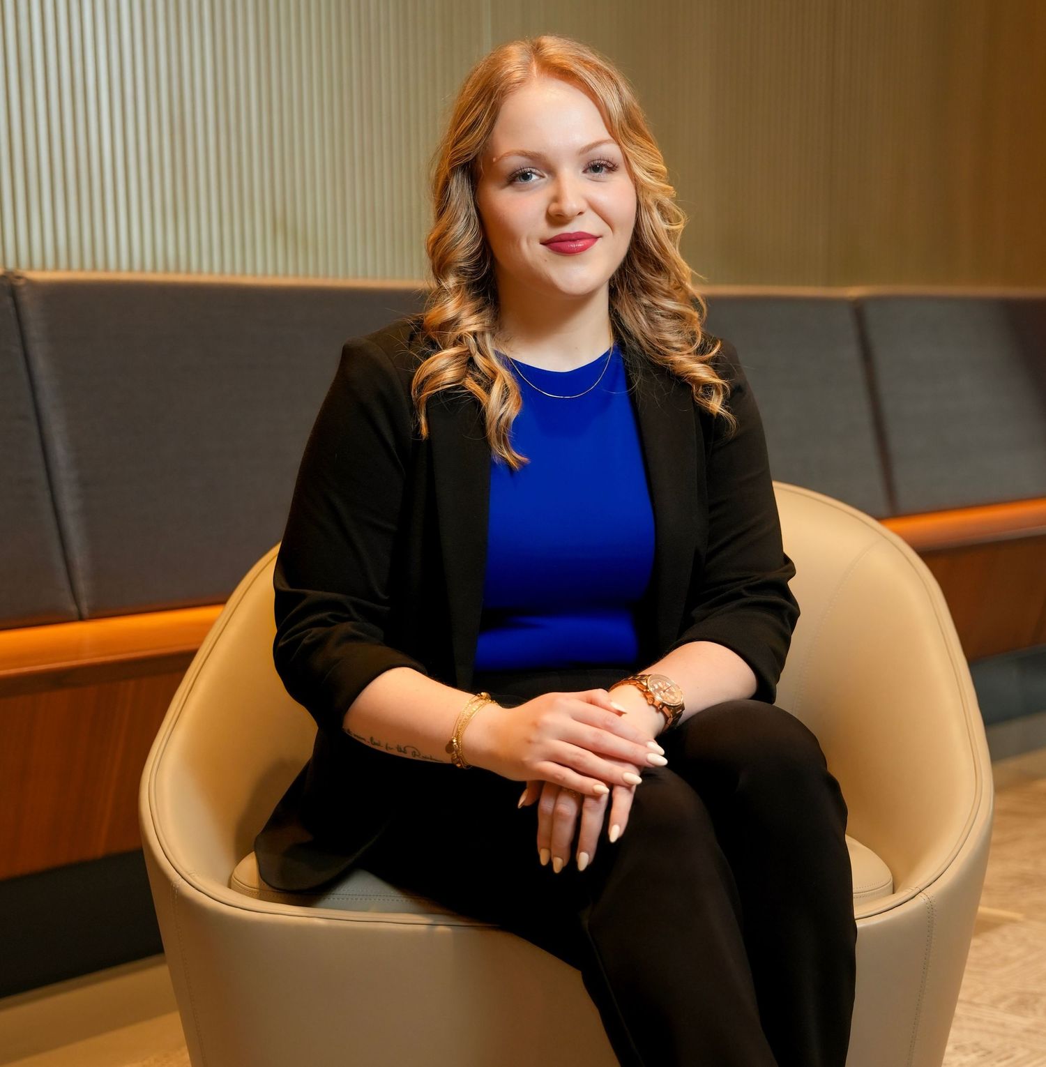 Professional seated in a black blazer and blue top against a neutral background.