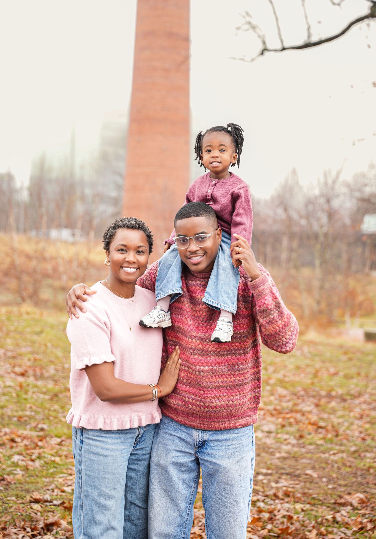 Autumn outdoor family portrait with children in pink and denim outfits among fallen leaves.