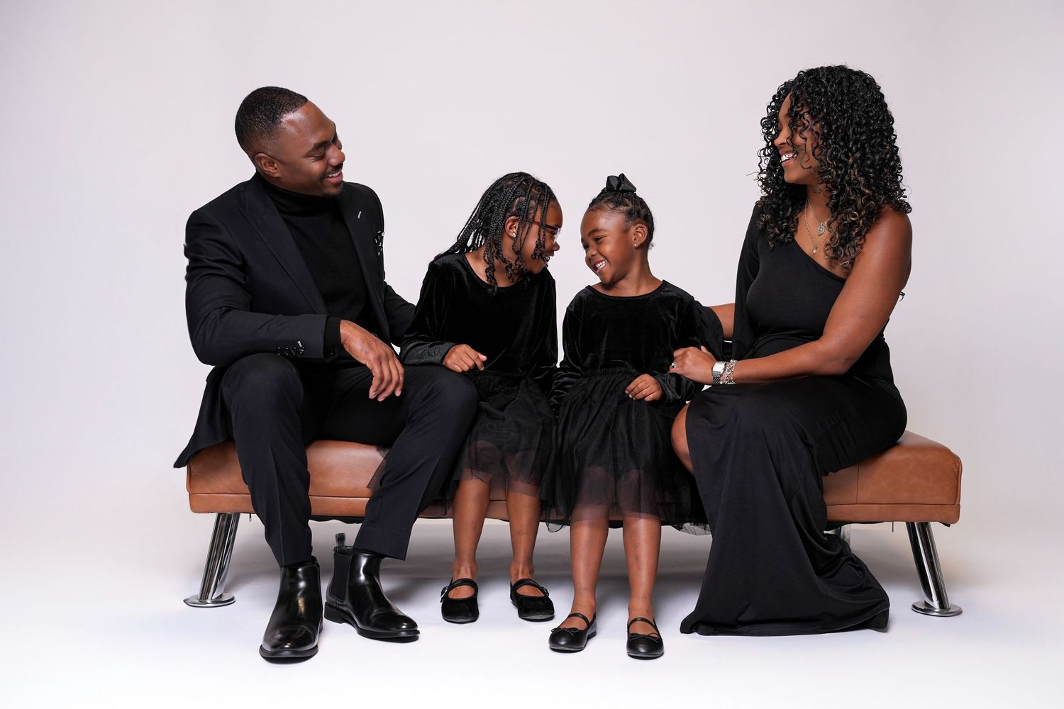 Family members in black outfits pose together on white background for stylish portrait session.