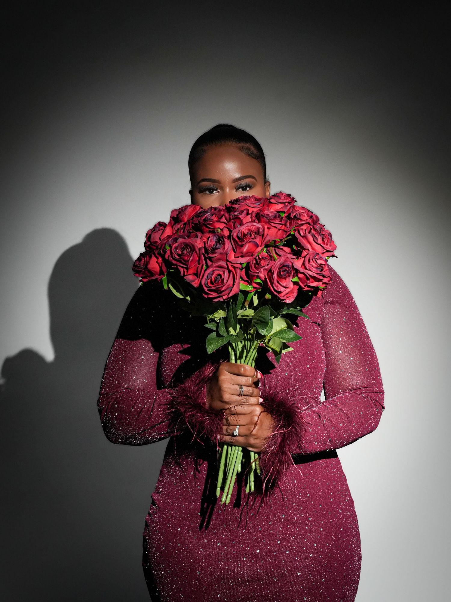 Figure in burgundy dress holds vibrant red roses against dramatic black and white backdrop.