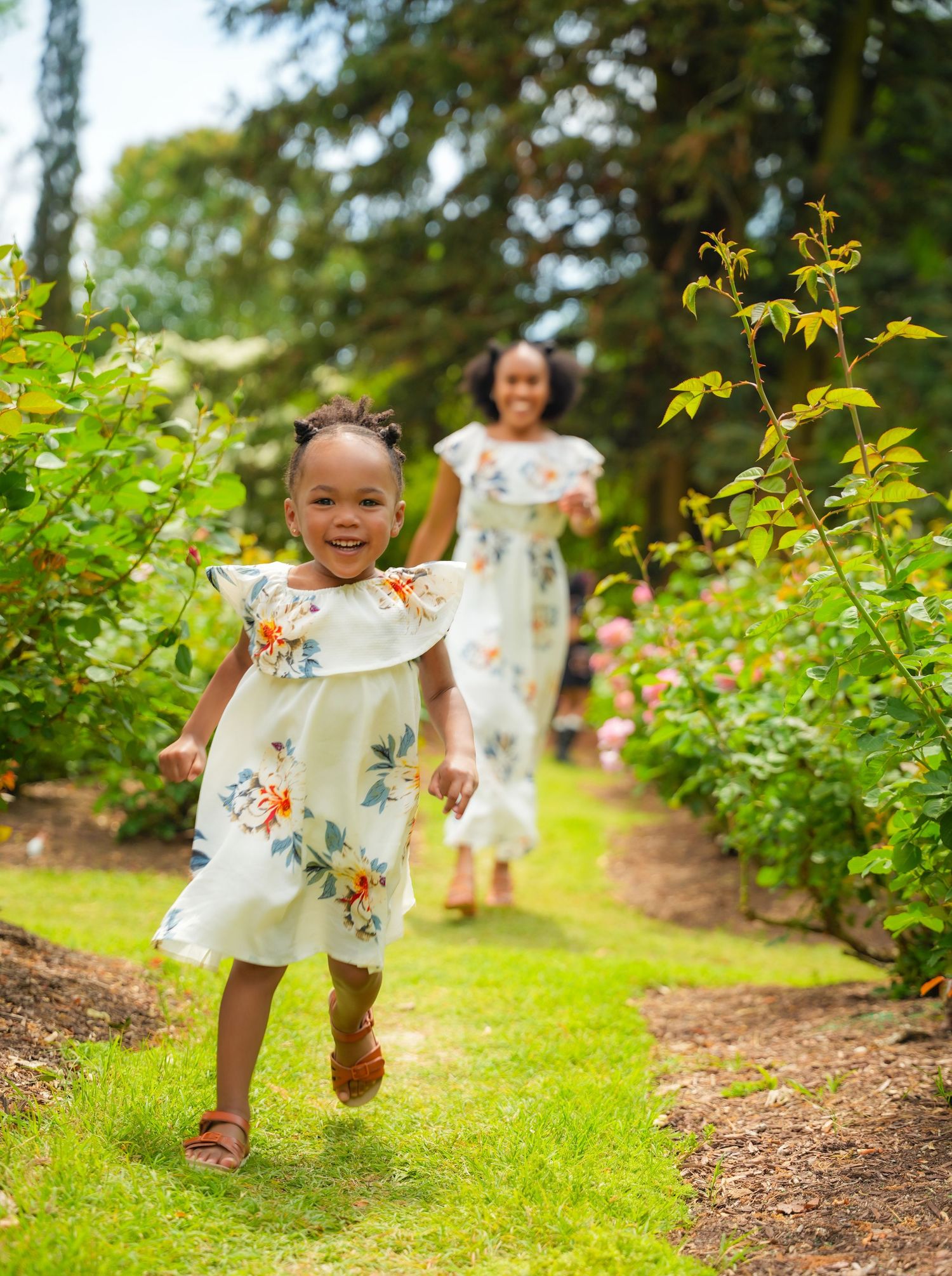 Young child in floral dress running and playing in garden pathway.