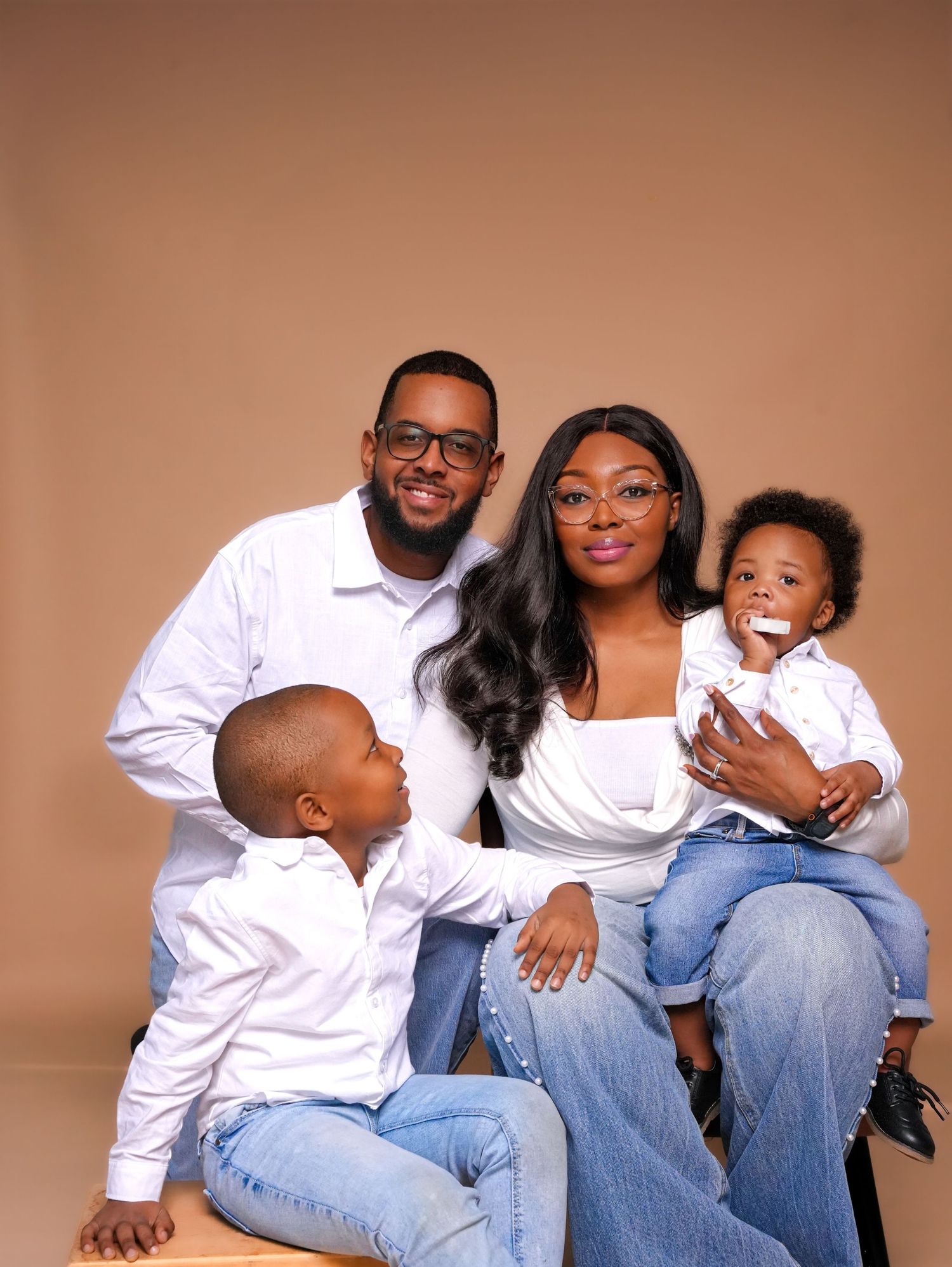 Family wearing white shirts and jeans poses together for casual studio portraits against brown background.
