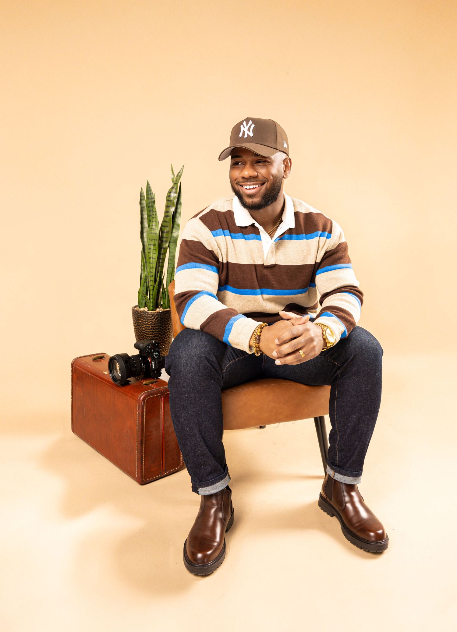 A person wearing a striped shirt and jeans sits casually on a wooden bench with a potted plant beside them.