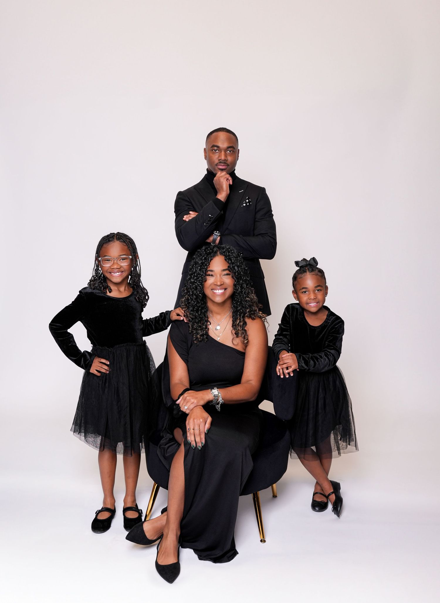 Elegant family portrait session with coordinated black outfits against white backdrop.