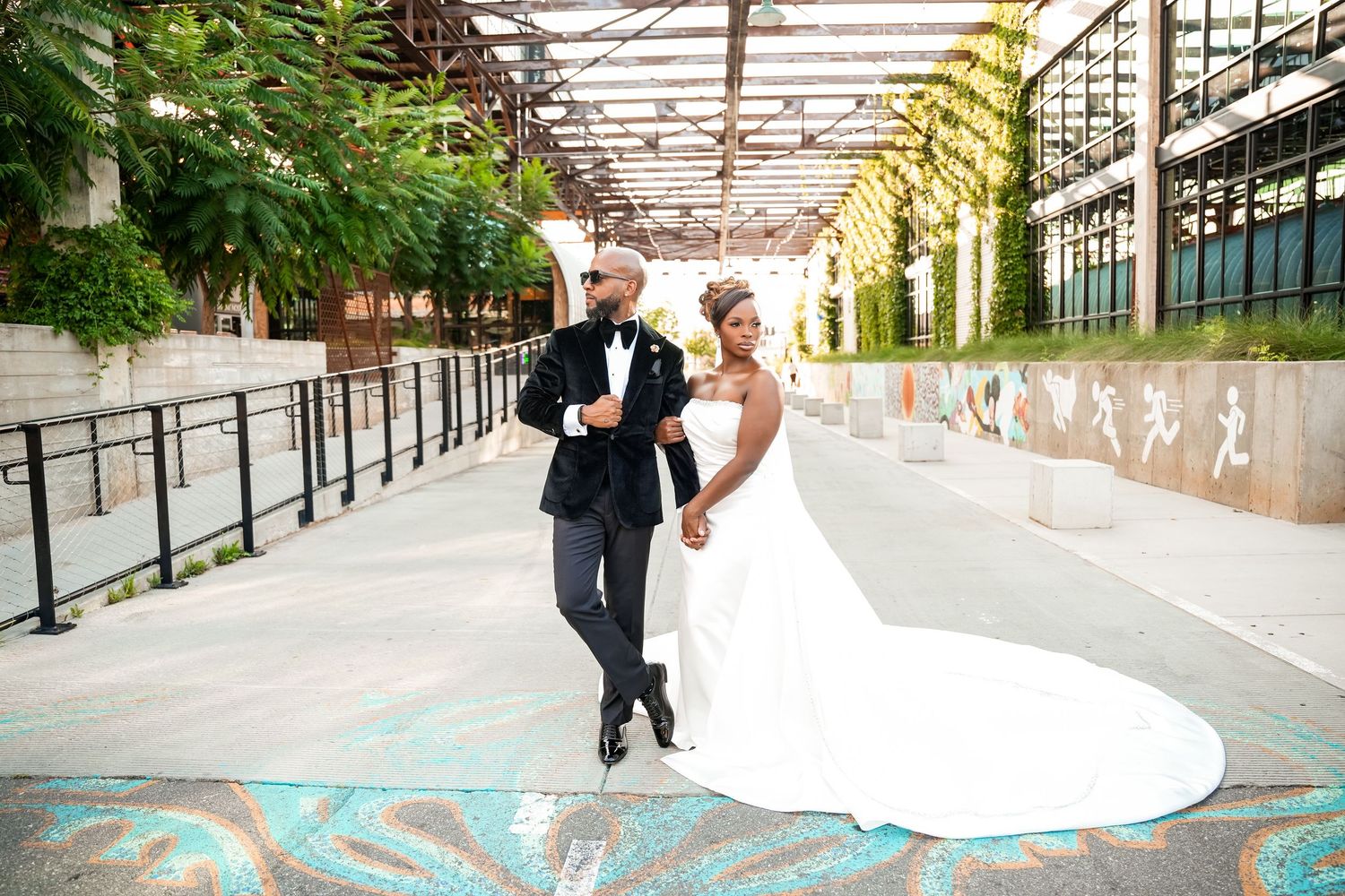 A couple in wedding attire dance together in an outdoor covered walkway with decorative wall art.