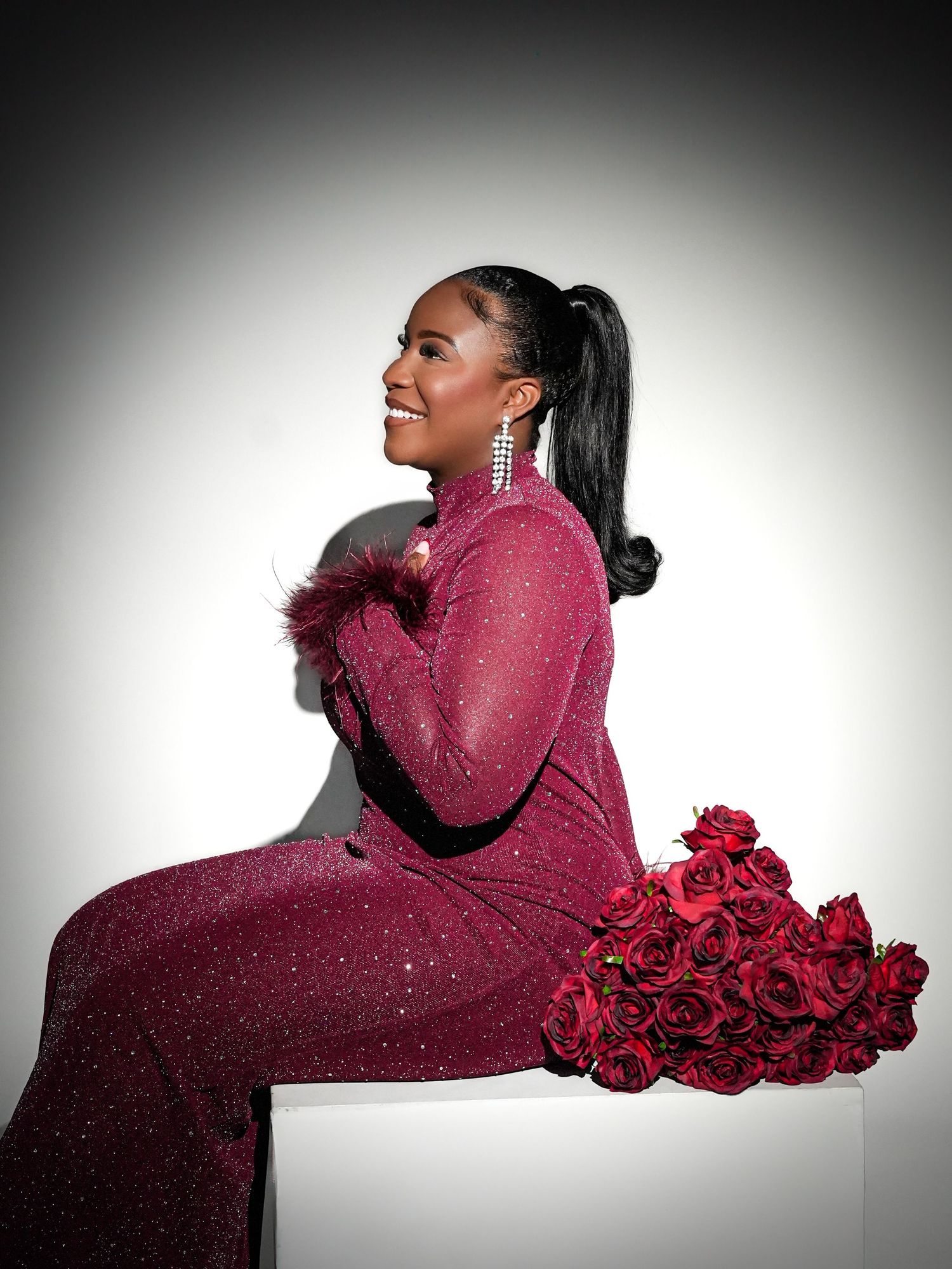 Dramatic fashion poses in burgundy sweater with cascading red roses against white background.