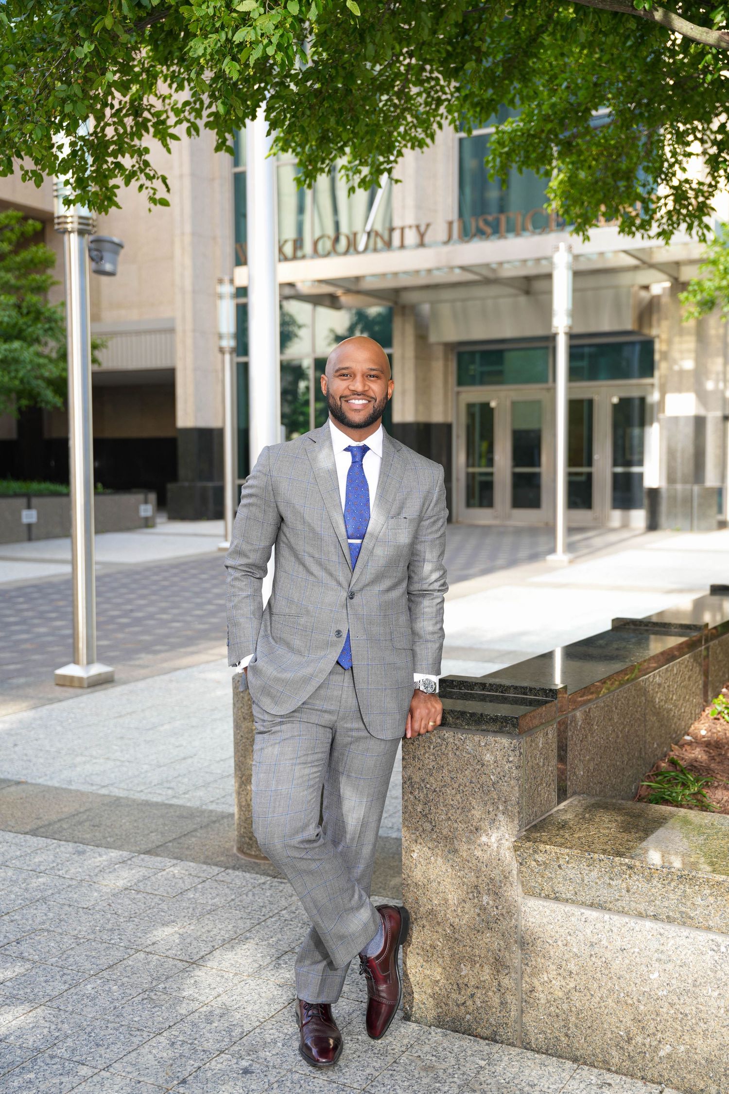 Professional Black businessman in gray suit and blue tie smiling outside a county justice building.