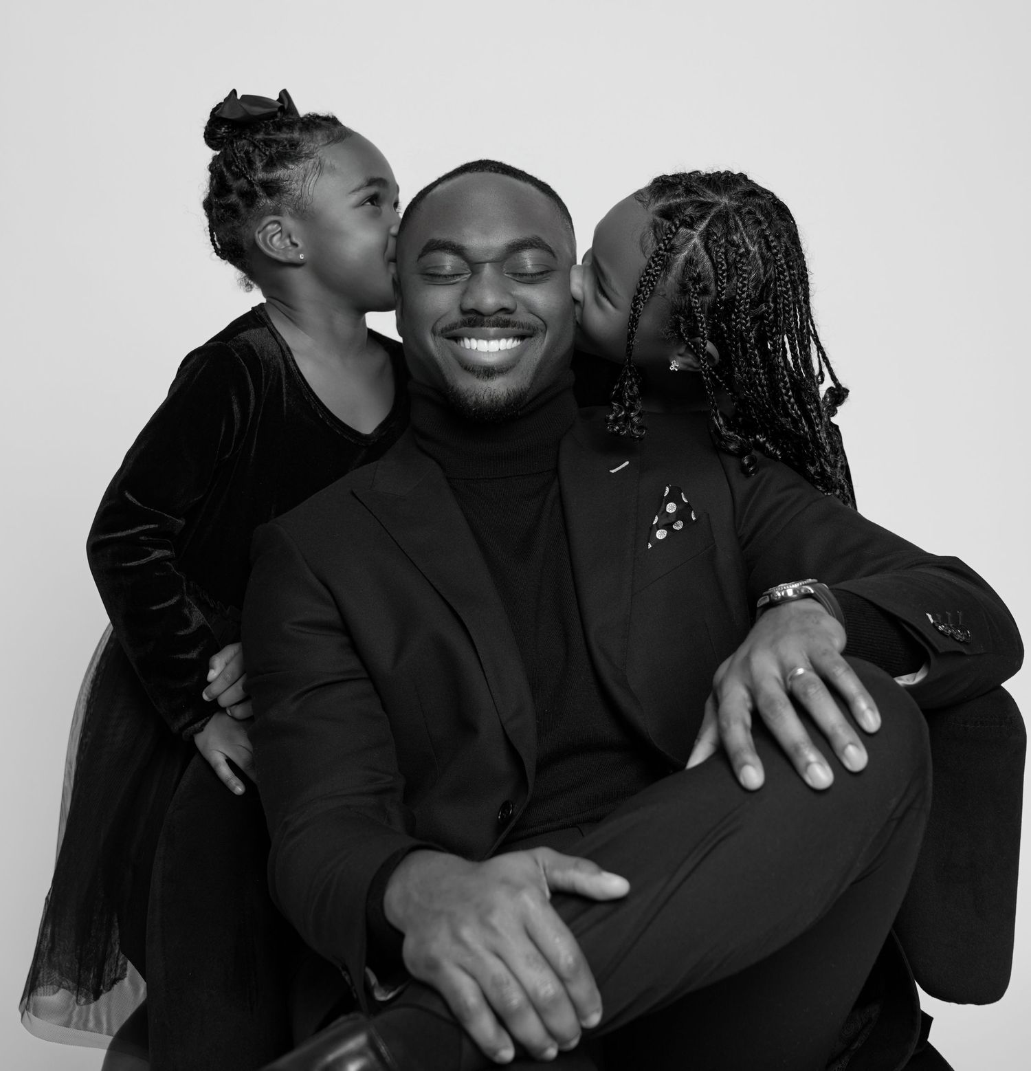 Family members embrace while wearing black formal attire against white studio background.