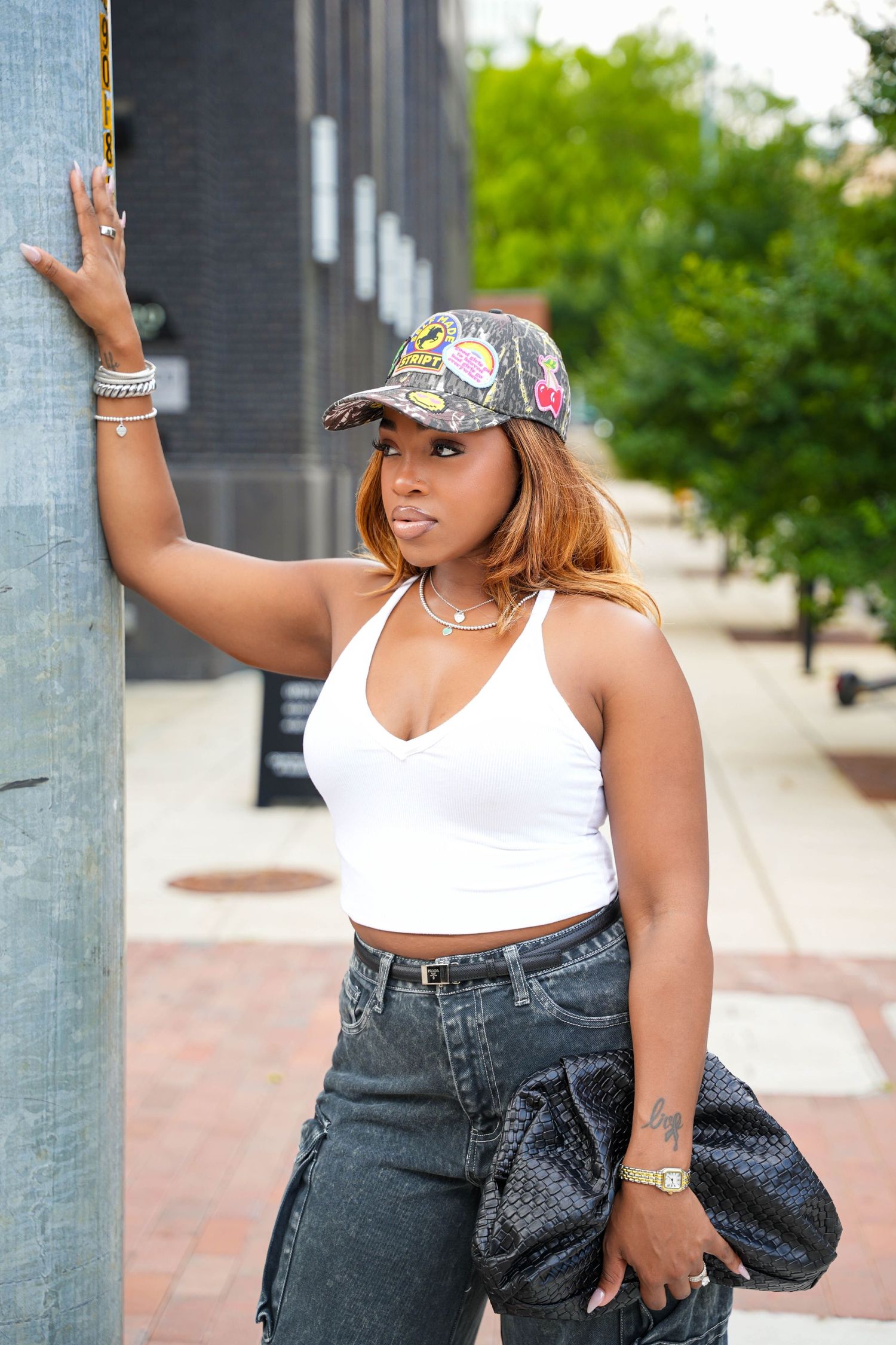 Stylish woman in white crop top, patterned cap, and dark jeans poses against urban pillar outdoors.