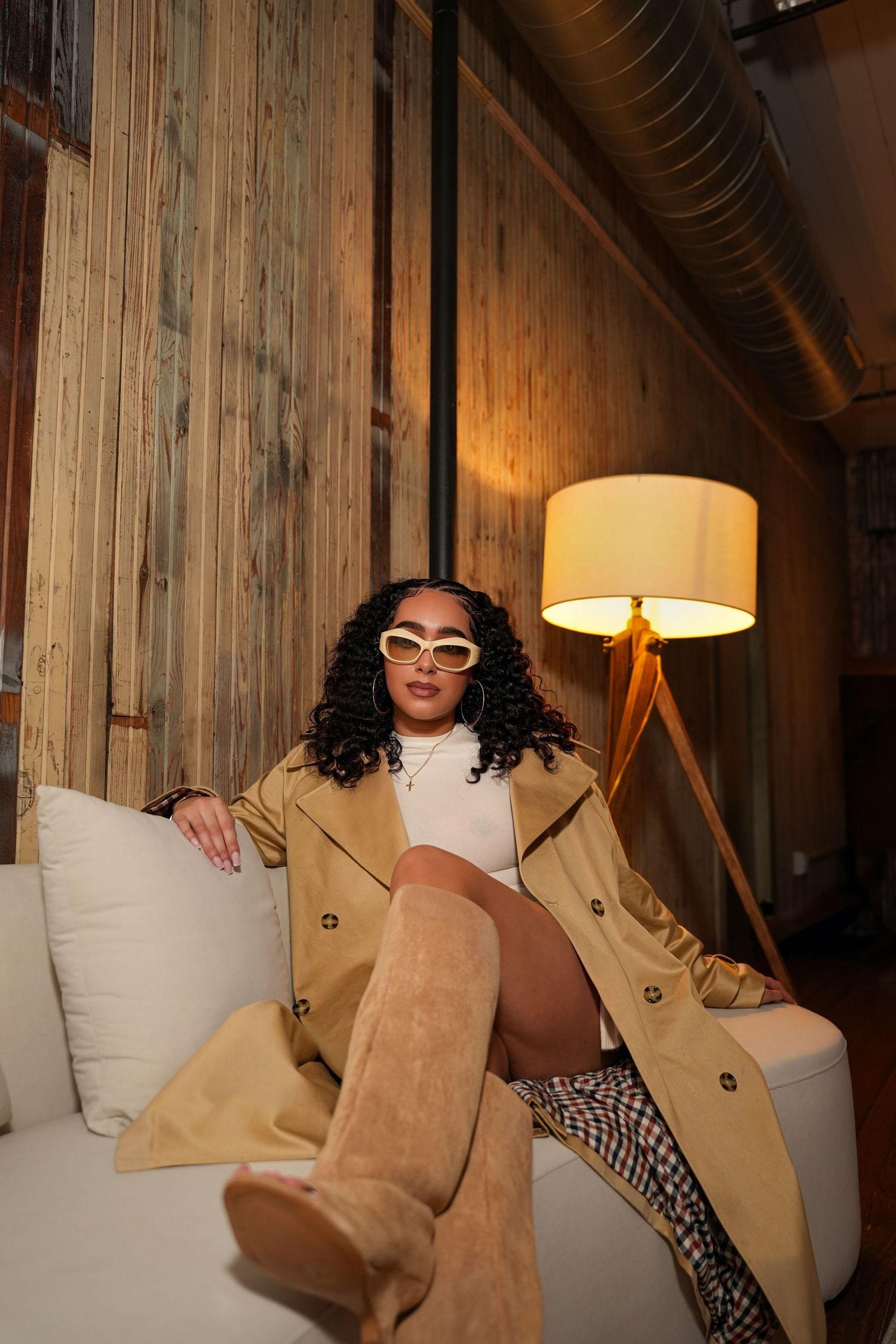 Fashion editorial shots on a white couch featuring a tan trench coat and sunglasses.