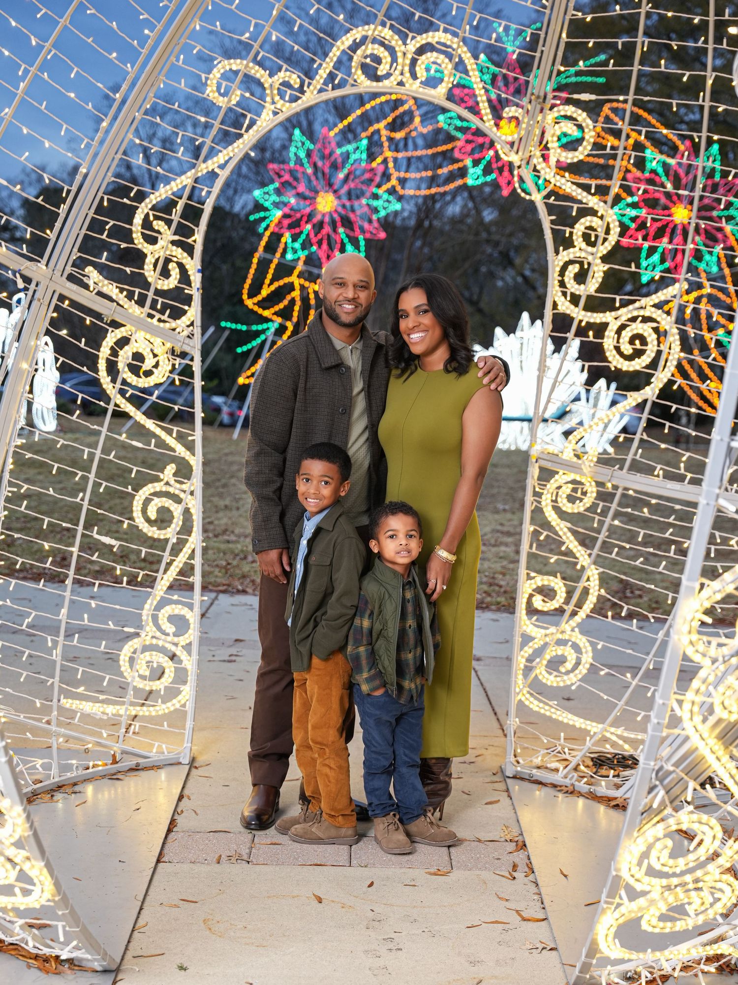 Family poses together in front of illuminated holiday light display outdoors.
