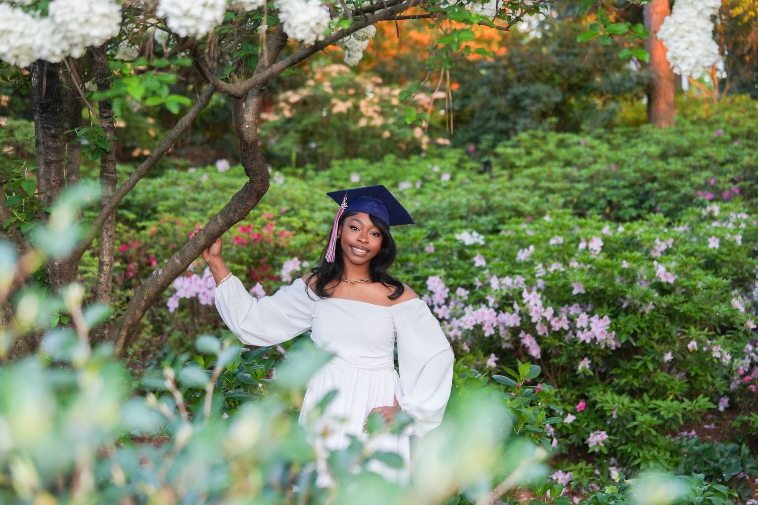 Outdoor maternity photography session among blooming white flowers and greenery.
