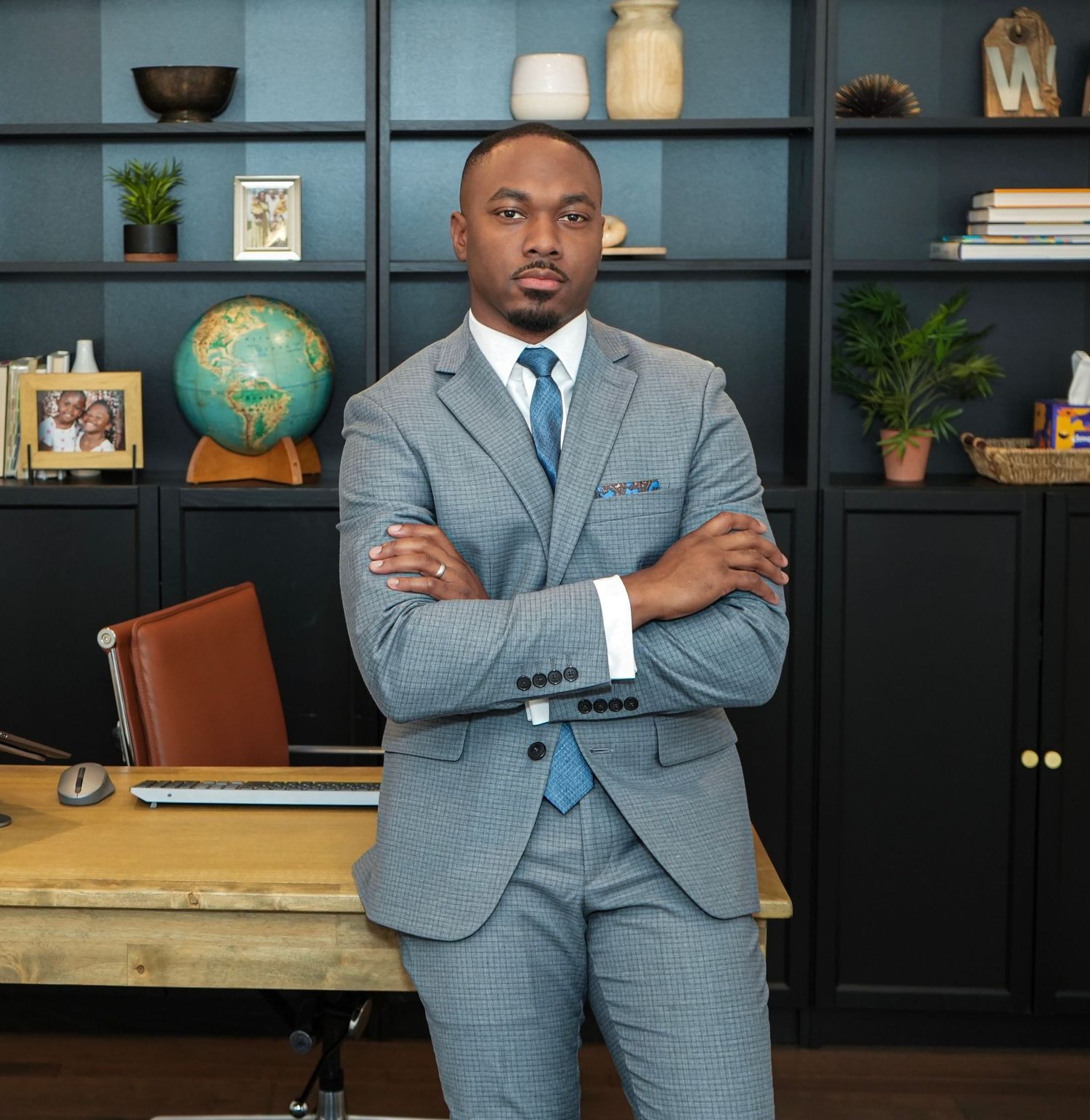 Business professional in gray suit photographed in modern office with bookshelves and decor.