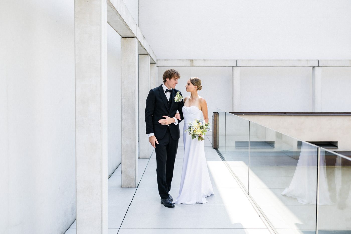 A bride and groom share a romantic moment in a modern architectural setting with white columns and clean lines.