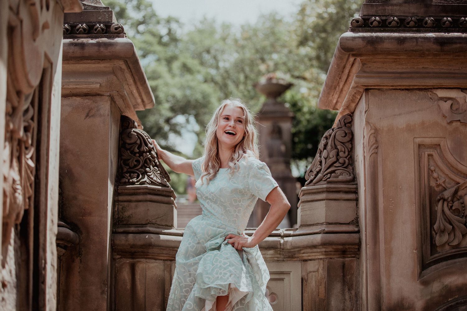 Blonde woman in mint lace dress posing between ornate stone pillars outdoors.