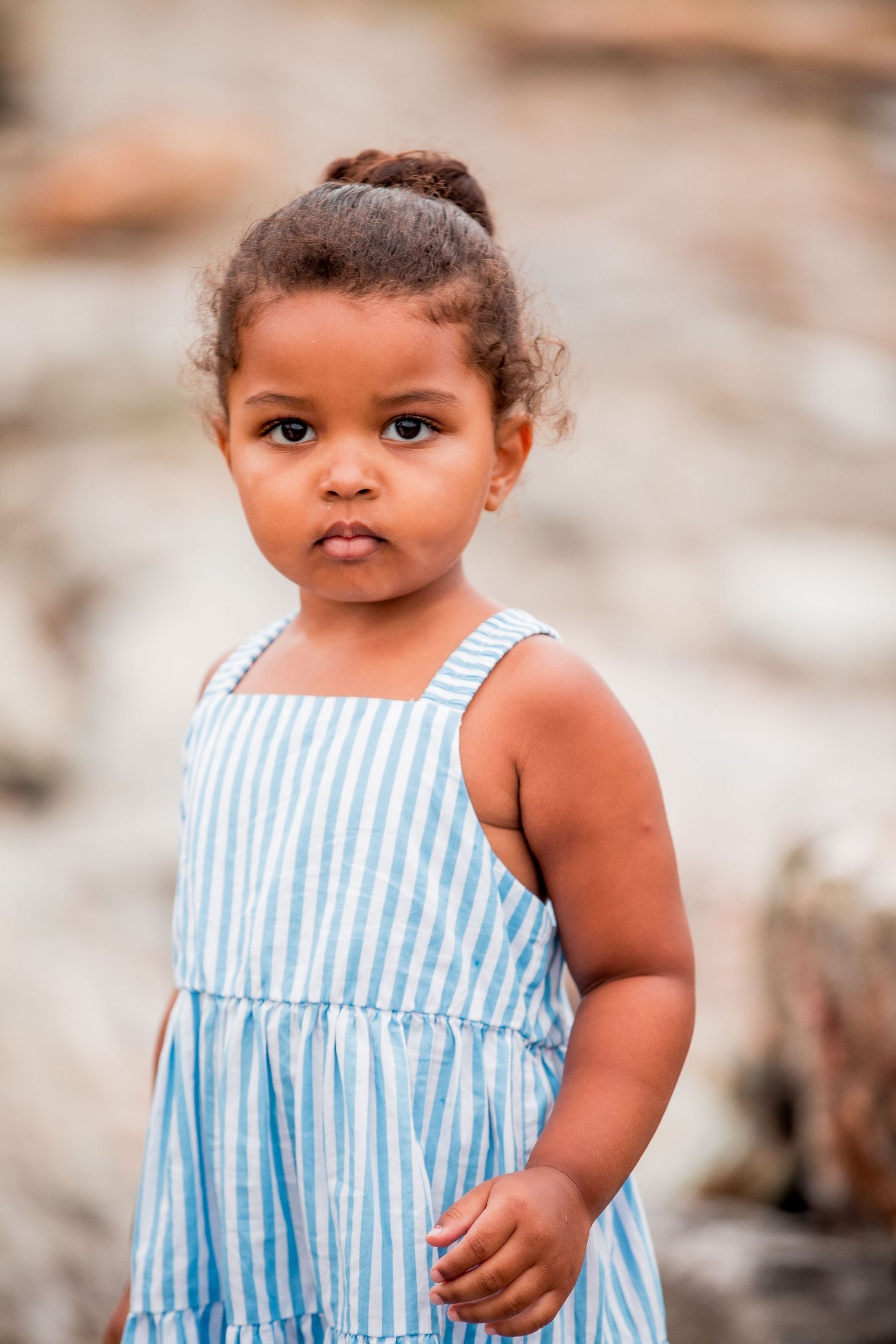 Close-up portrait of a toddler girl in a blue striped sundress outdoors.