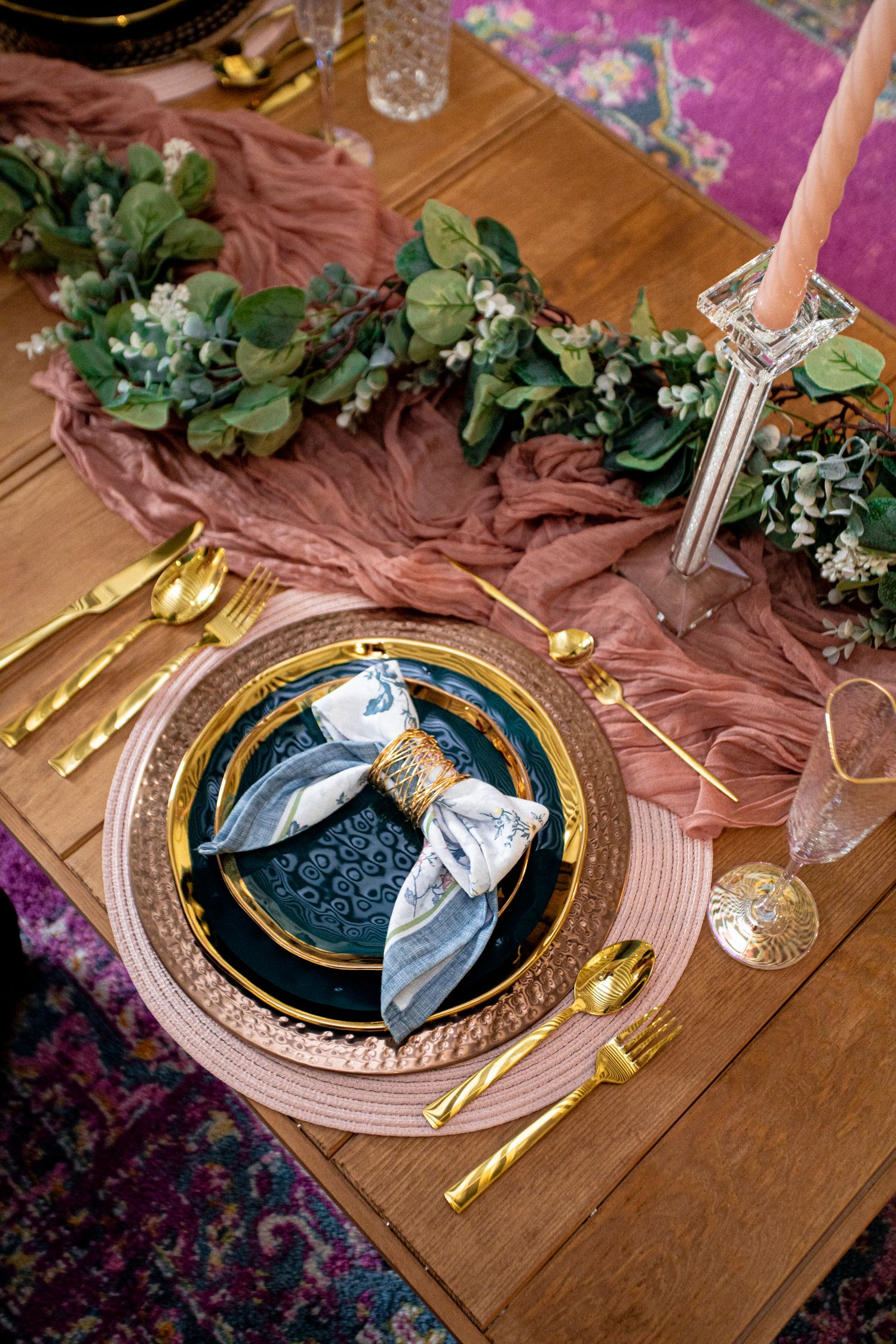 Elegant table setting with gold cutlery, navy plates, pink placemat, floral garland, and a draped dusty rose table runner.