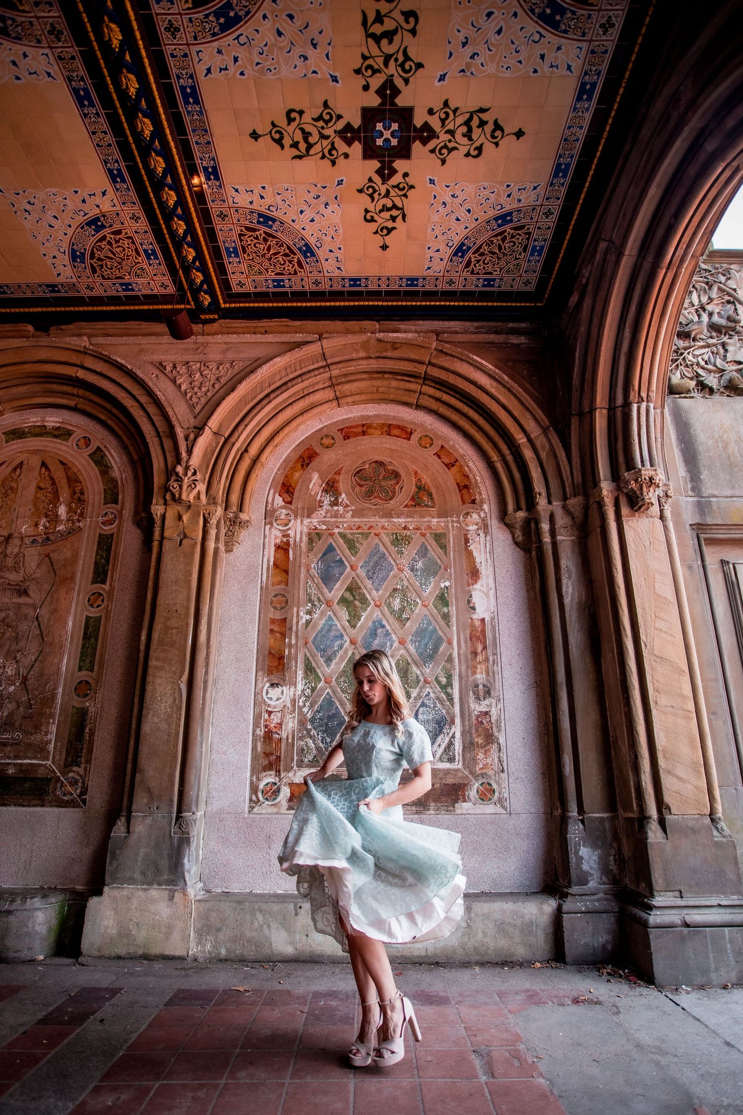 Young woman in light blue tulle dress twirling inside the ornate Bethesda Terrace arcade in Central Park.