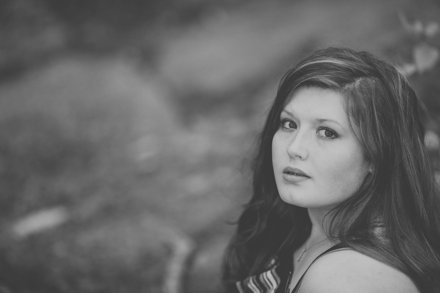 Black and white portrait of a young woman with long dark hair gazing at the camera outdoors.
