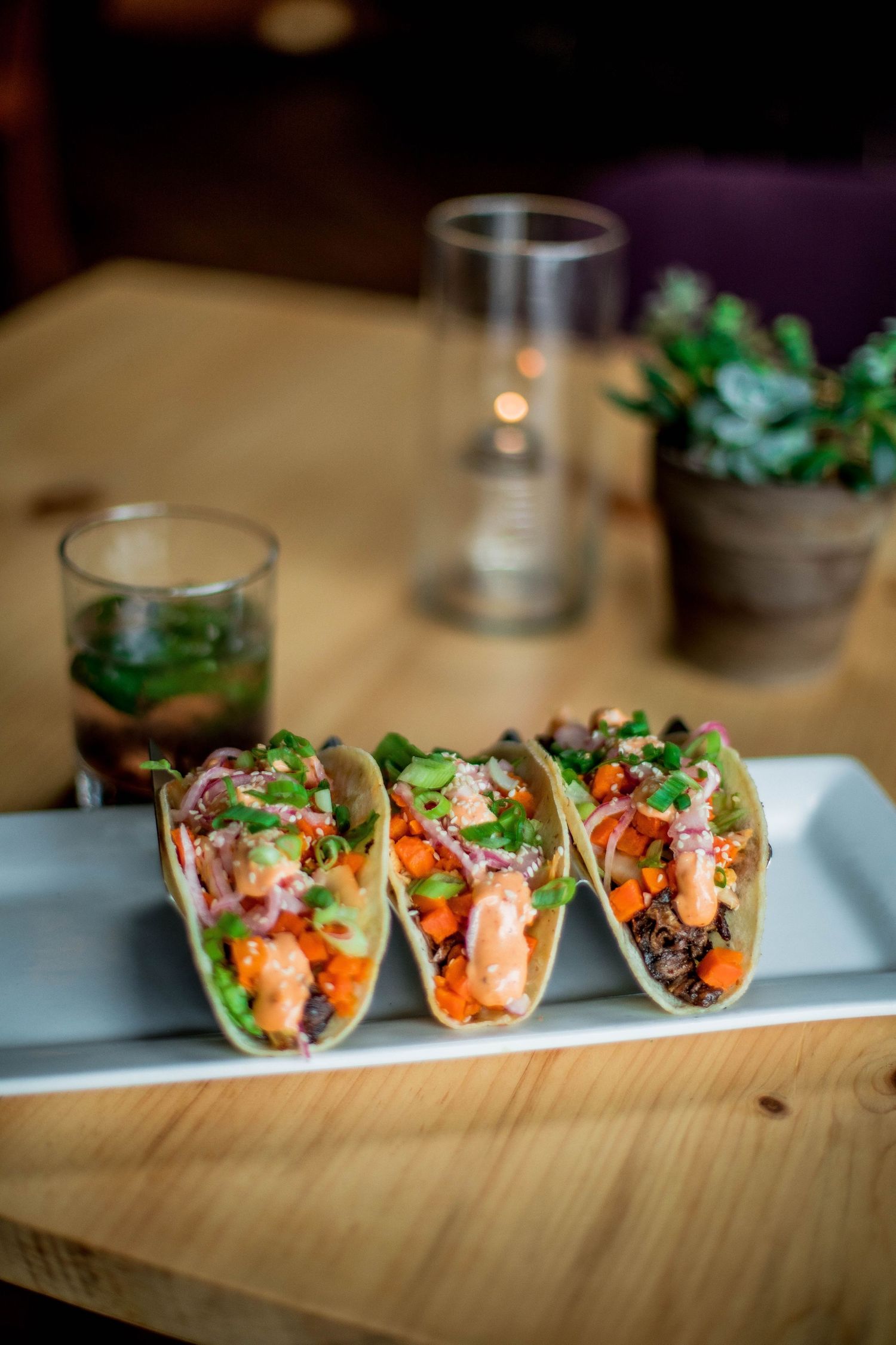 Three colorful shrimp tacos with fresh vegetables served on a white rectangular plate at a restaurant.