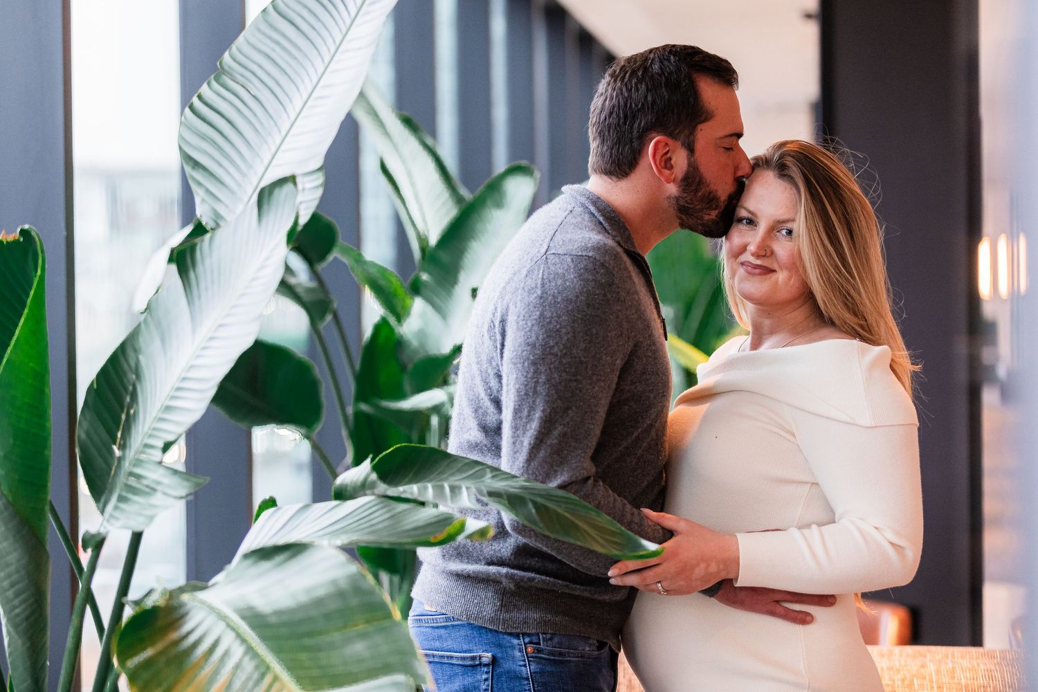 Couple sharing tender moment near tropical plants during maternity photo session.
