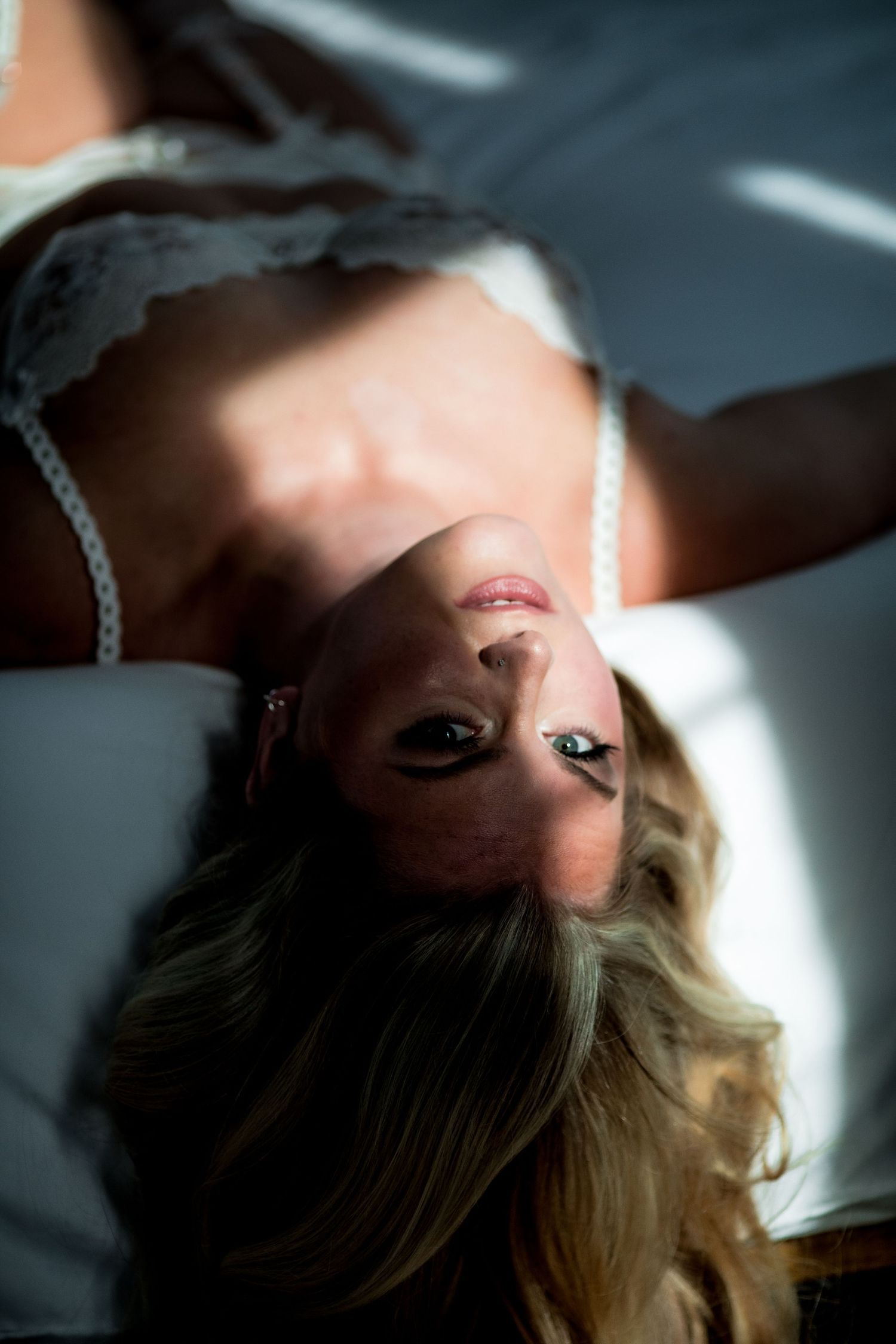 Blonde woman in white lace lingerie lying back on bed looking up.