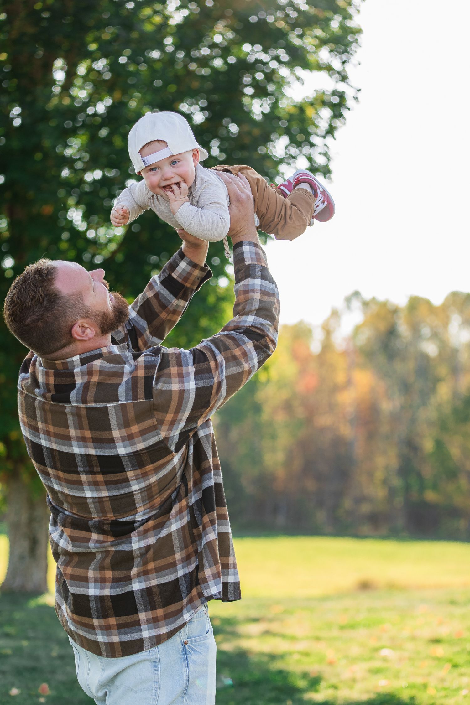 Father lifting smiling baby in the air outdoors in autumn park during golden hour.