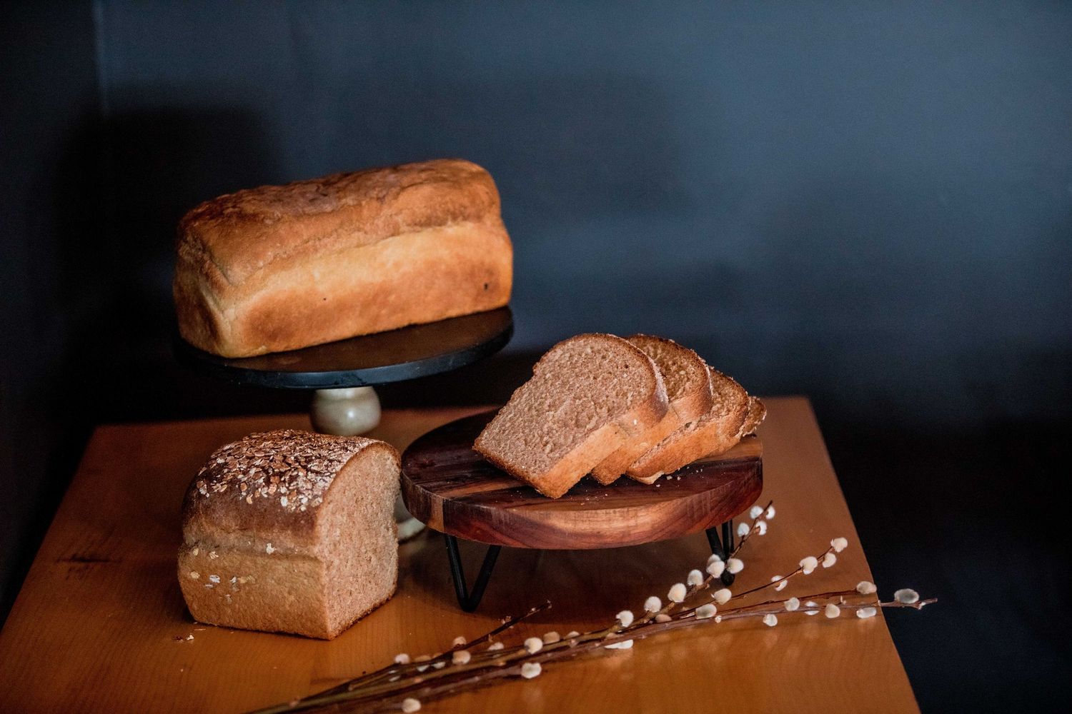 Assorted artisan bread loaves and slices displayed on wooden boards with decorative branches.