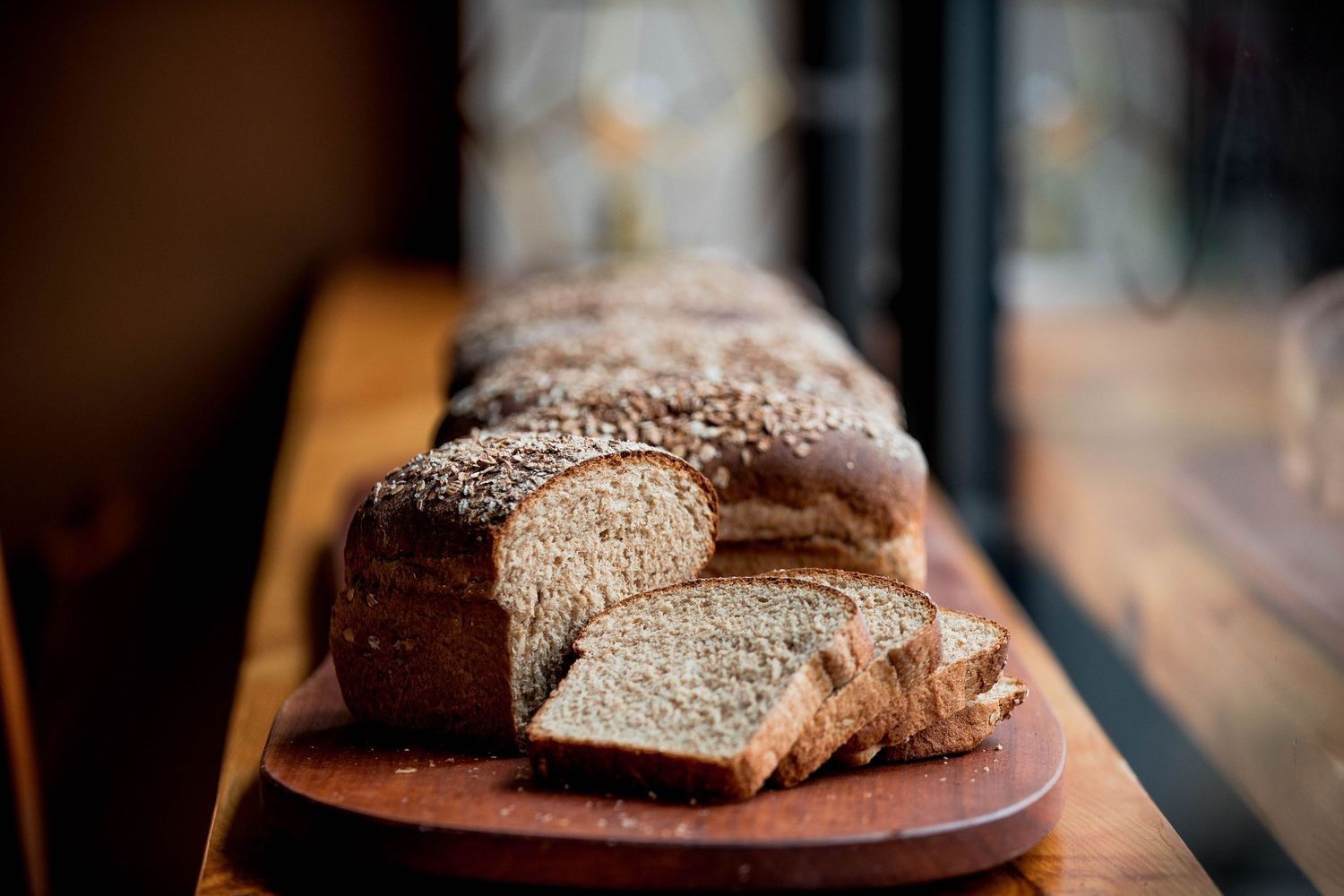 Freshly sliced whole grain bread loaf on a wooden cutting board by a window.