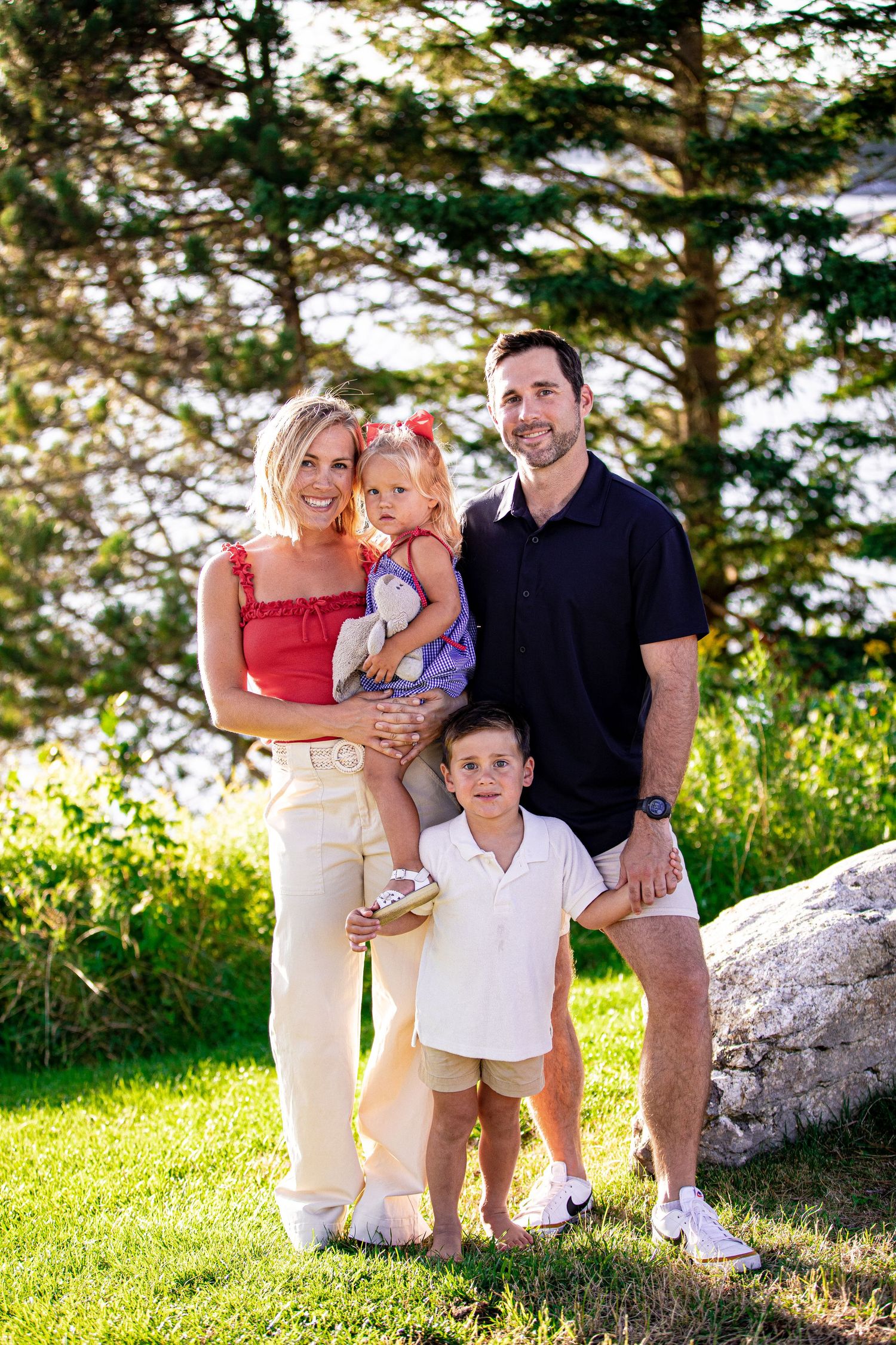 Happy family of four posing outdoors near trees with two young children in summer on Cape Cod.