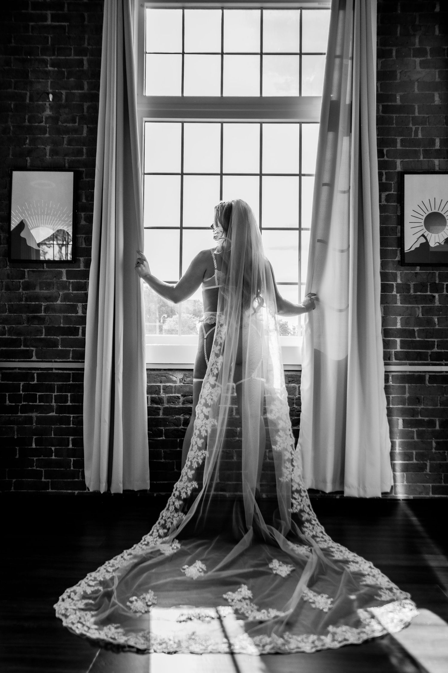 Black and white silhouette of bride in veil standing before large window.