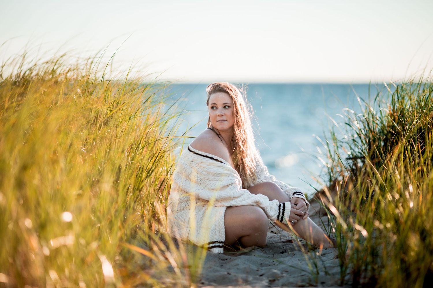 Young blonde woman sitting in Cape Cod beach grass dunes near the ocean.